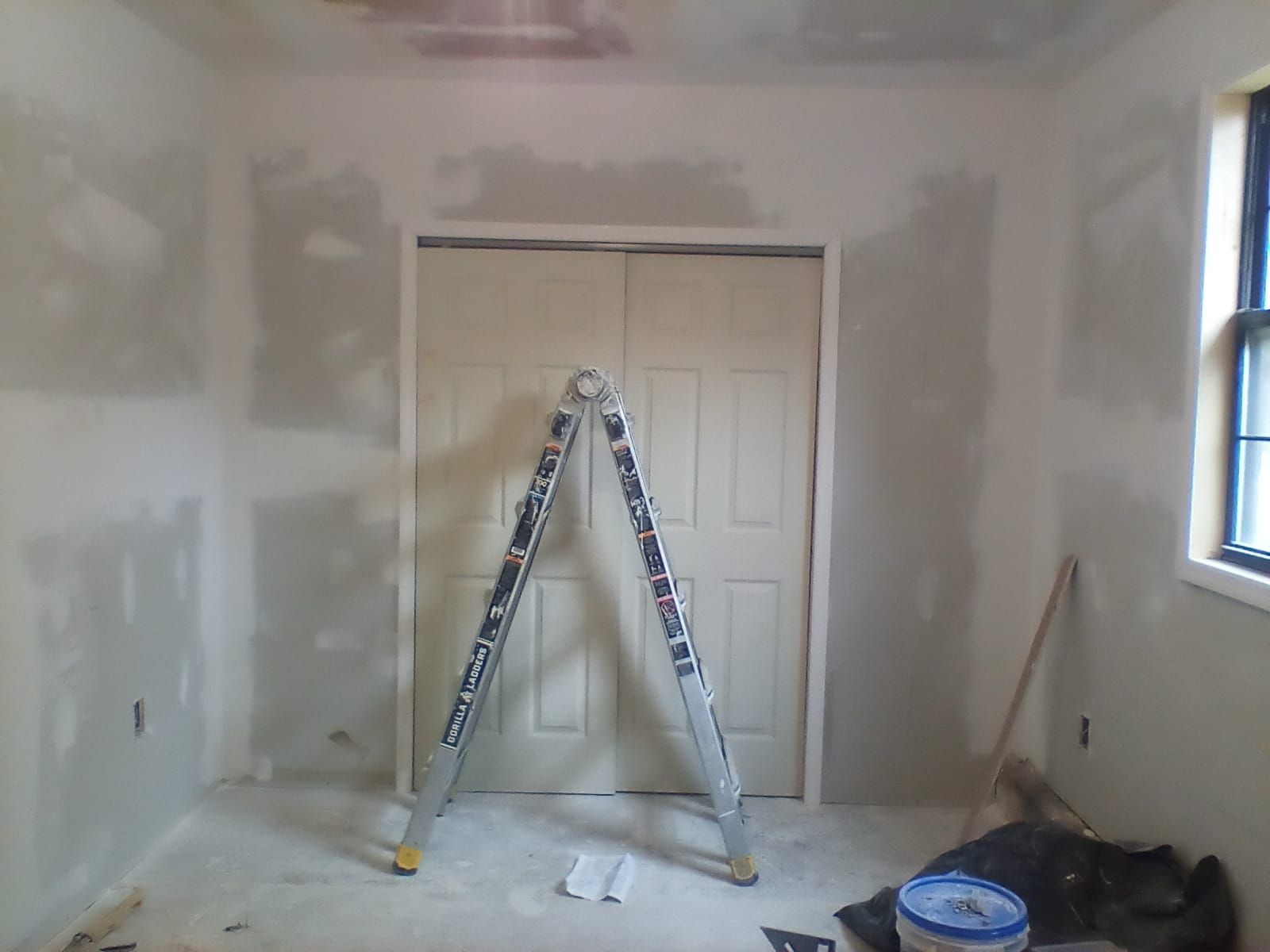 Partially finished room with drywall patching, a ladder in front of closet doors, and tools on the floor