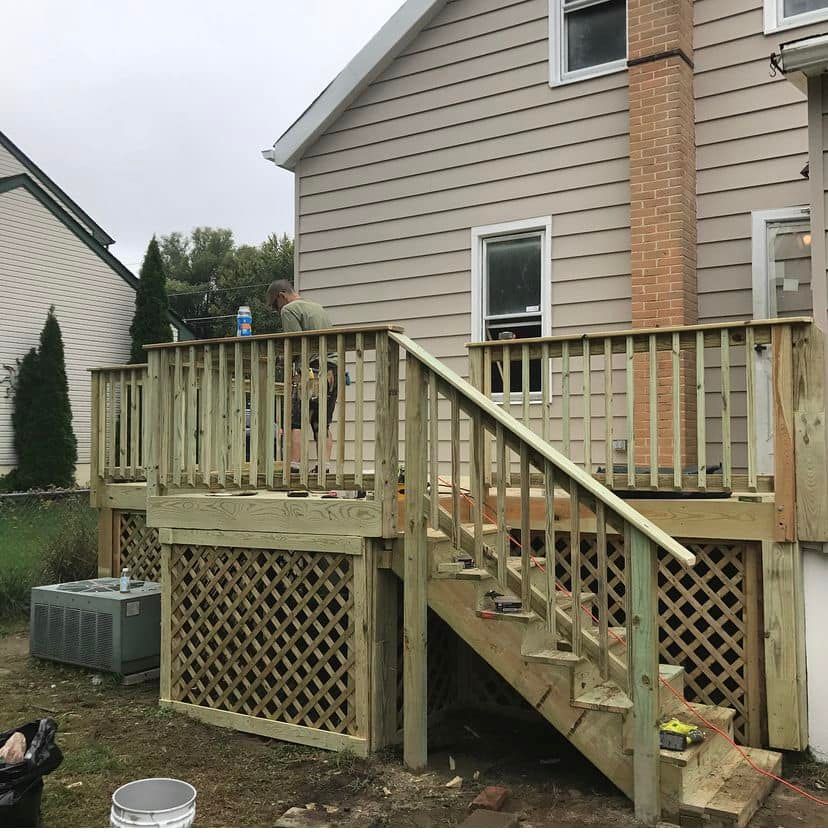 Back deck with wooden stairs and railing attached to a beige house