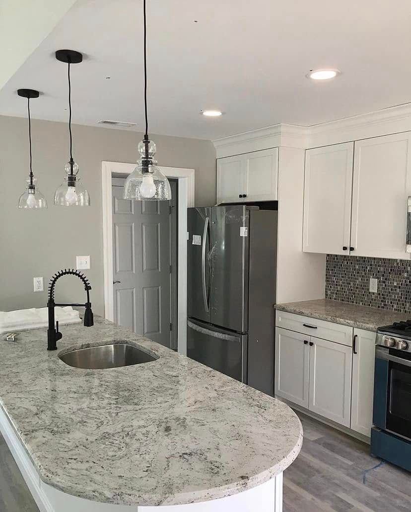 Bright modern kitchen with granite island, stainless steel appliances, white cabinets, and pendant lights