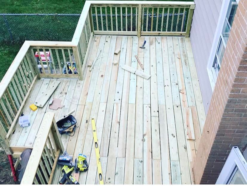 Wooden deck under construction with tools, boards, and partially built railings beside a brick house