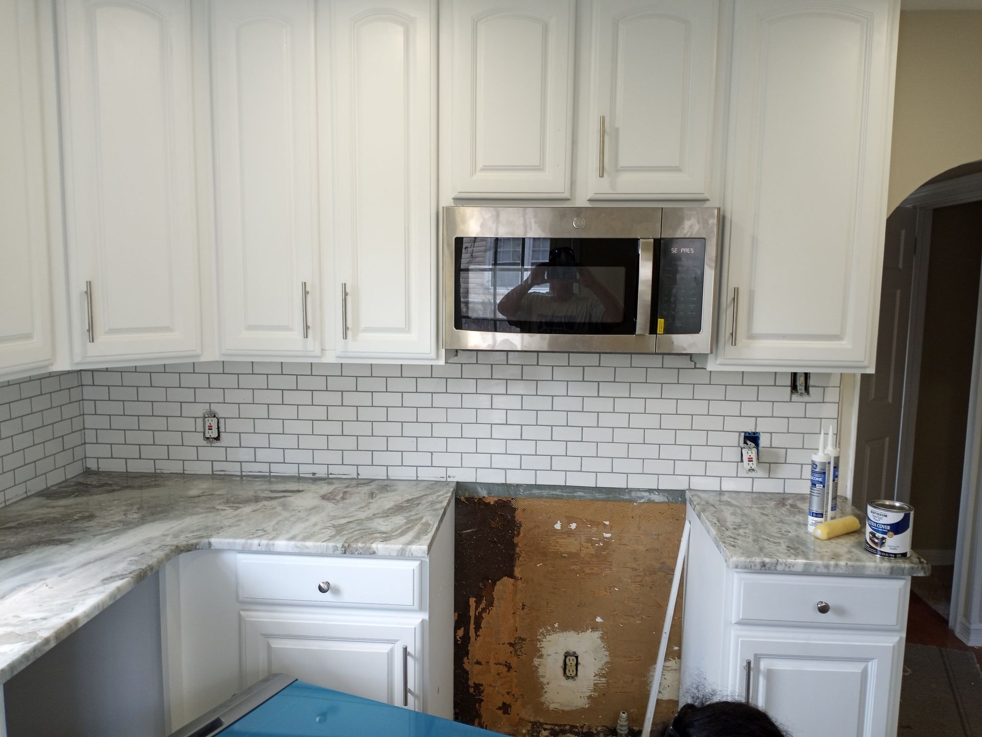 Kitchen with white cabinets, gray countertops, subway tile backsplash, and a built-in microwave above a missing stove area.