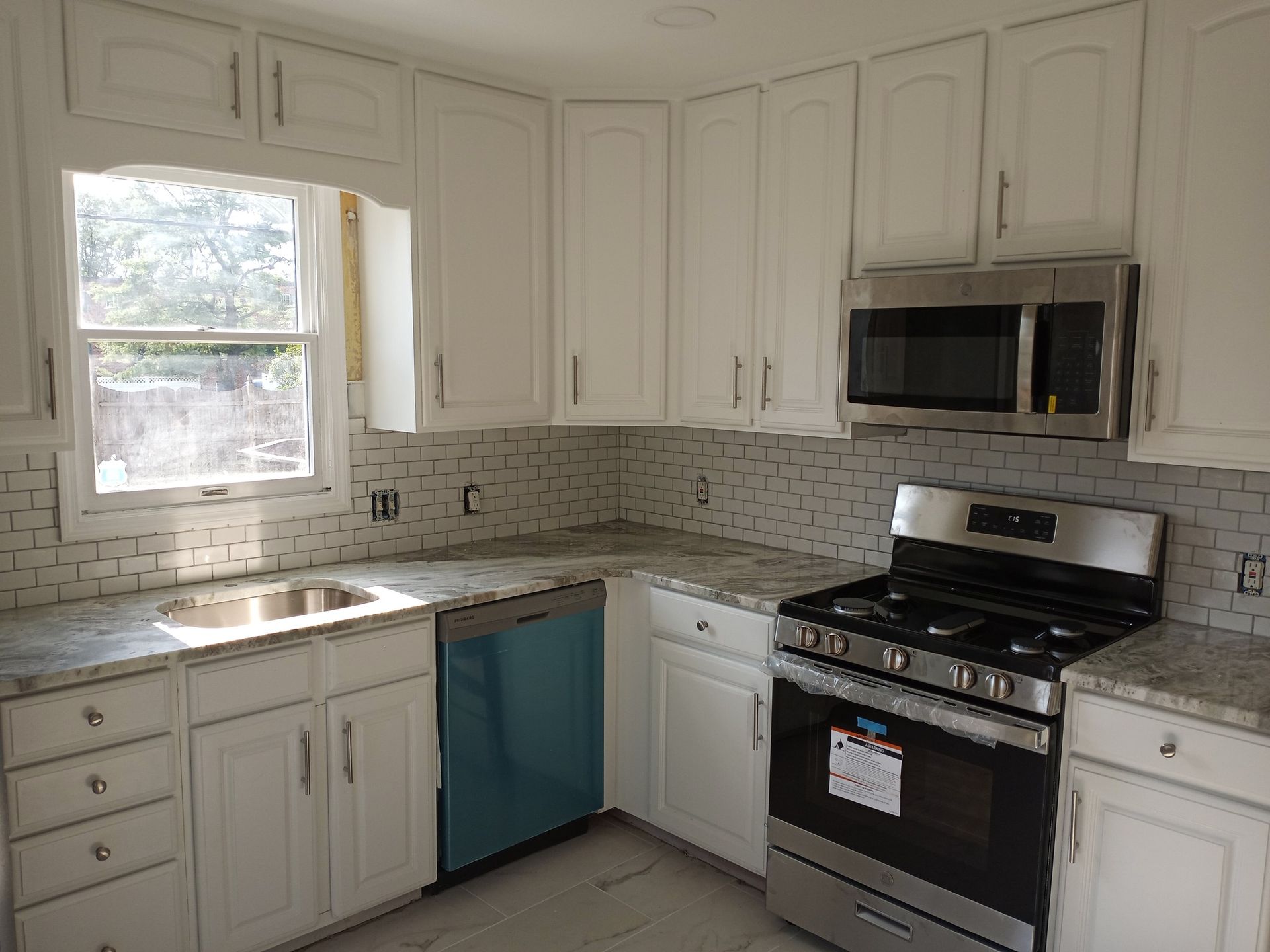 Bright kitchen with white cabinets, tiled backsplash, window over sink, and stainless steel stove and microwave.