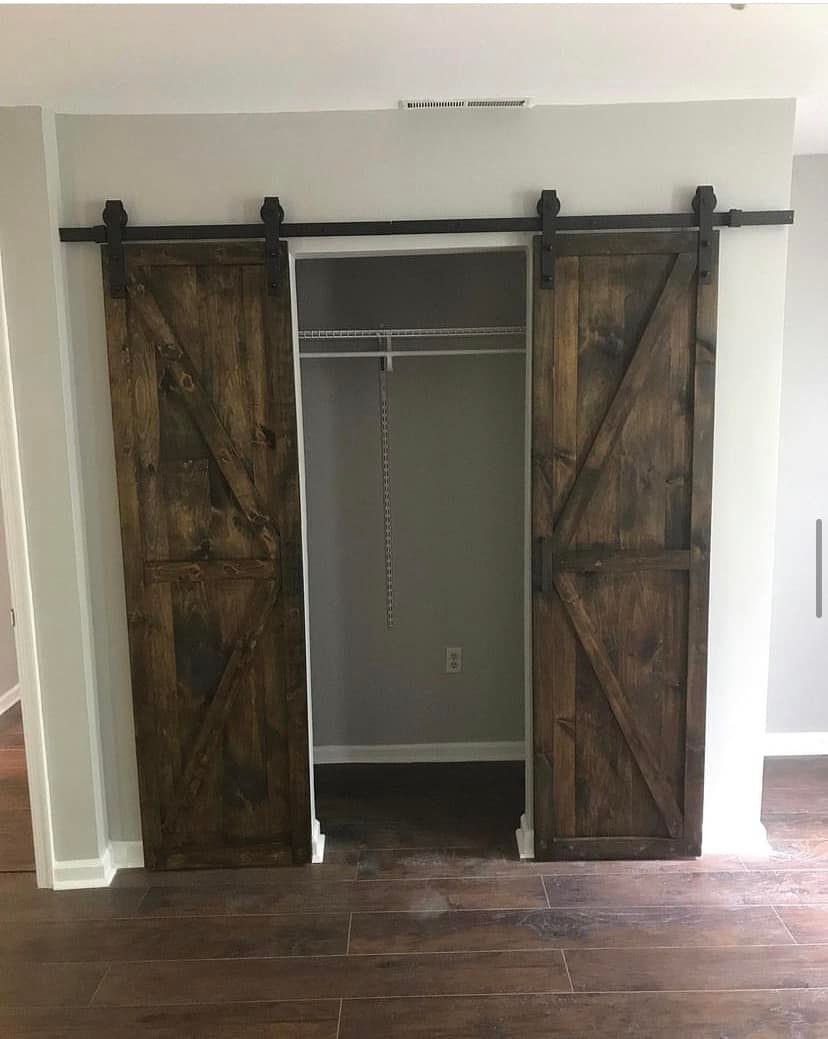 Rustic sliding barn doors framing a small closet opening in a room with dark wood flooring.