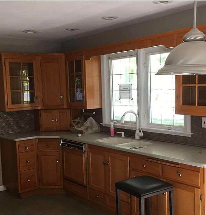 Wooden kitchen with corner cabinets, white sink by a bright window, and a black stool by the counter.