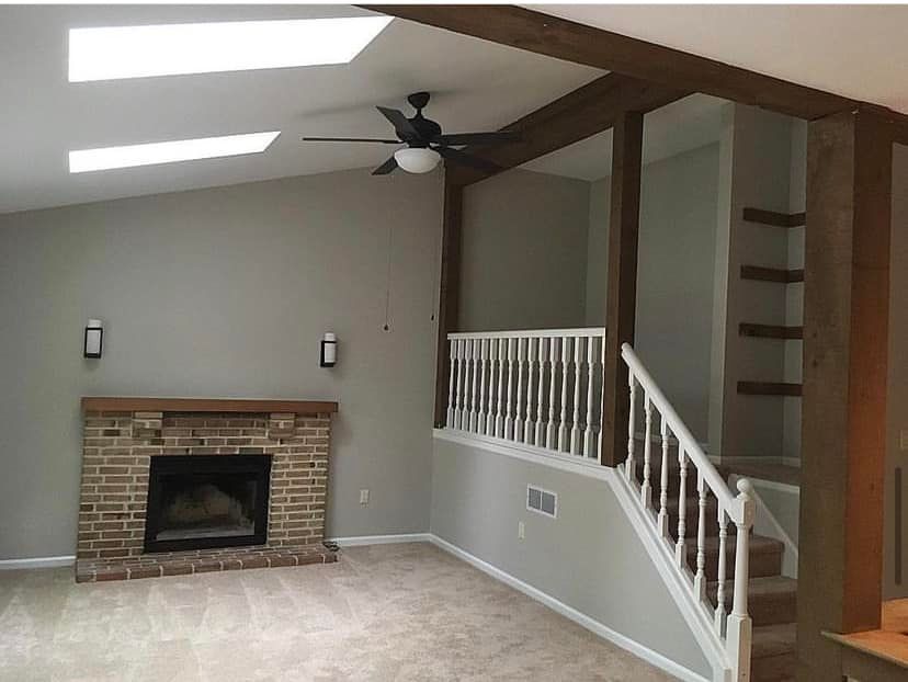 Living room with brick fireplace, vaulted ceiling, ceiling fan, and white staircase railing
