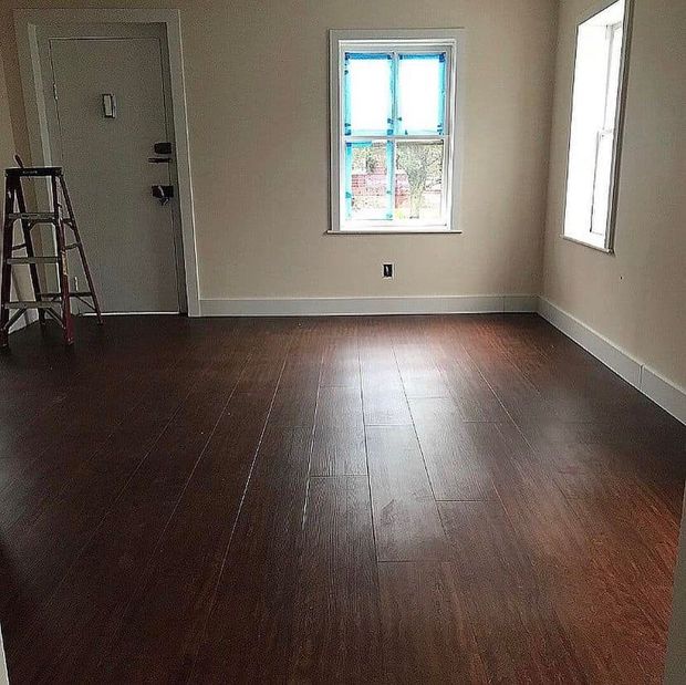Empty room with dark hardwood floors, beige walls, two windows, and a ladder near the door.