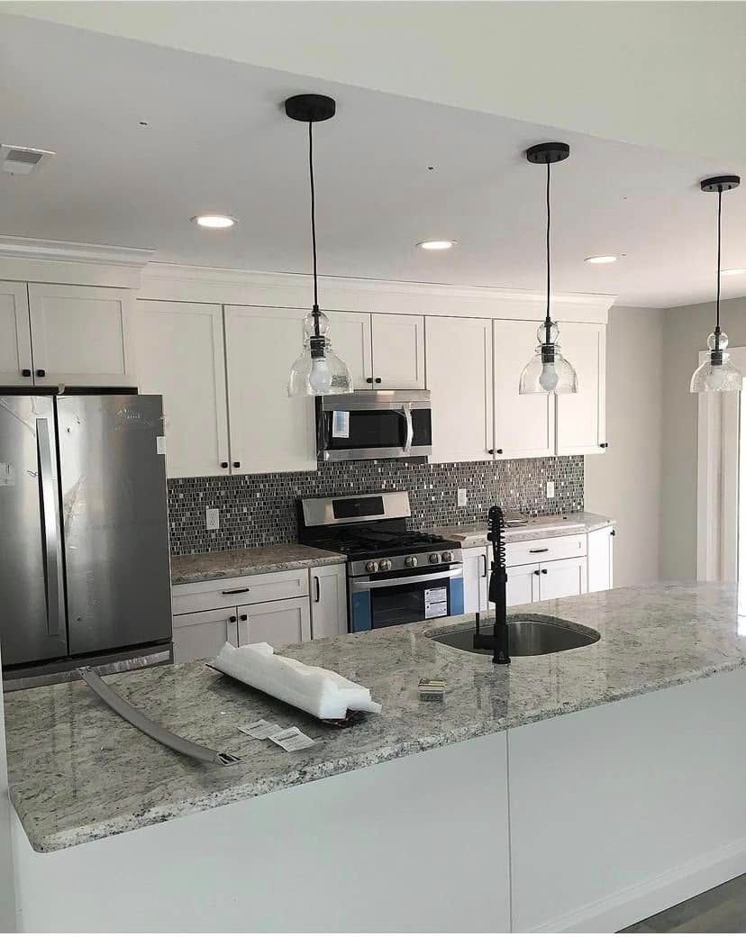 Modern white kitchen with granite island, stainless steel appliances, pendant lights, and tiled backsplash