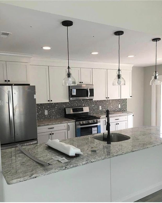 Modern kitchen with white cabinets, granite island, stainless steel appliances, and hanging pendant lights
