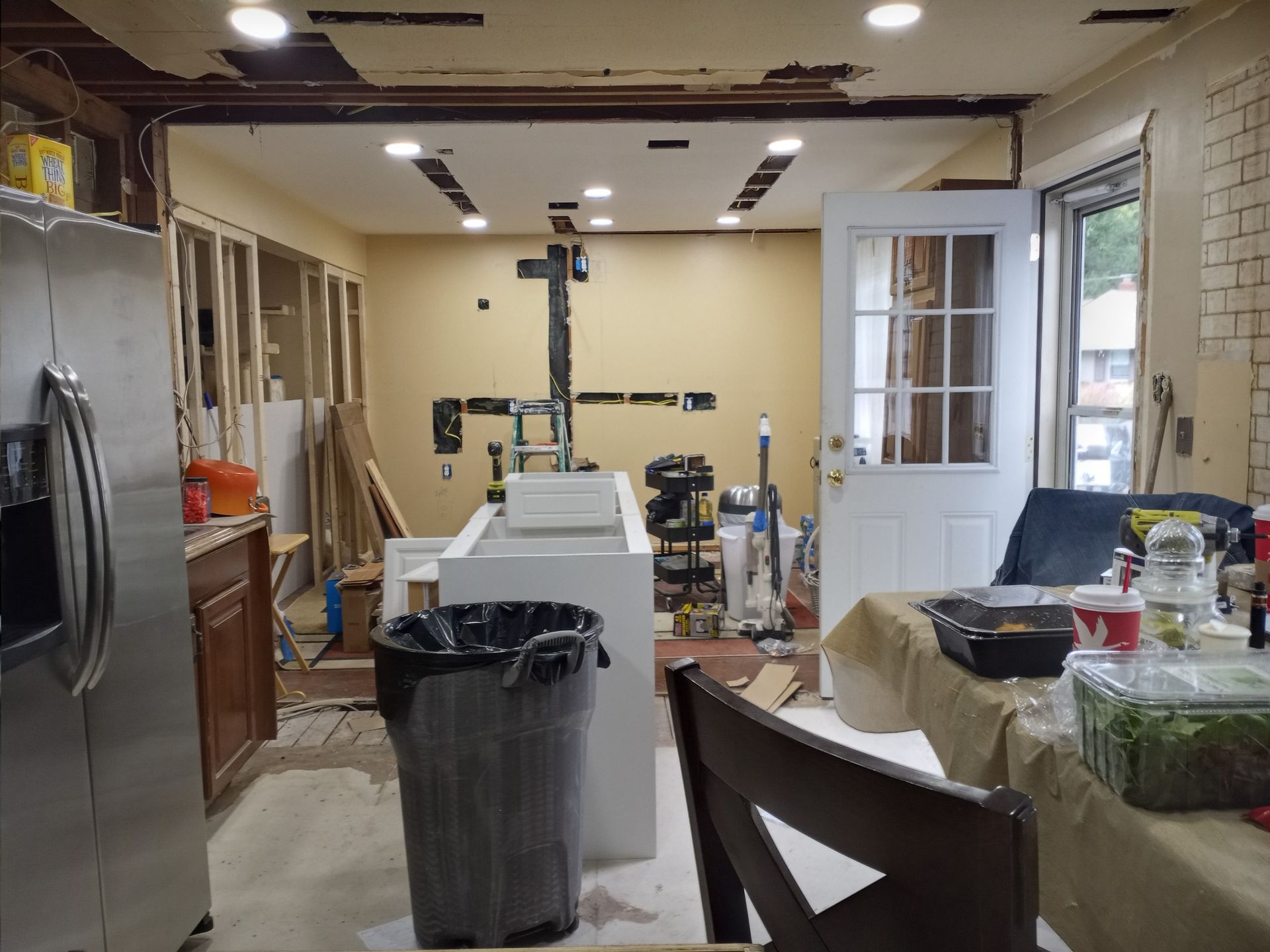 Renovated kitchen with stainless fridge, unfinished ceiling, tools, and supplies scattered around