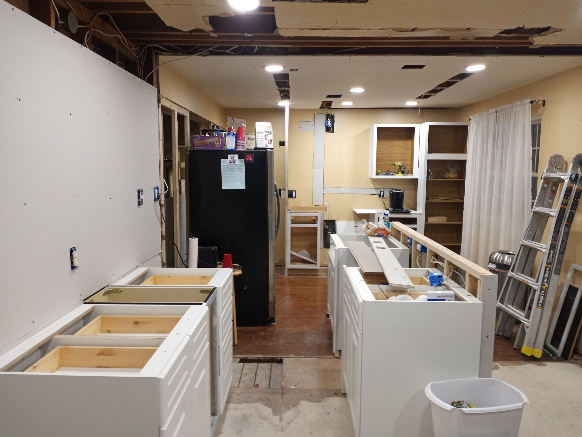 Renovated kitchen under construction with white cabinets, tools, and exposed ceiling