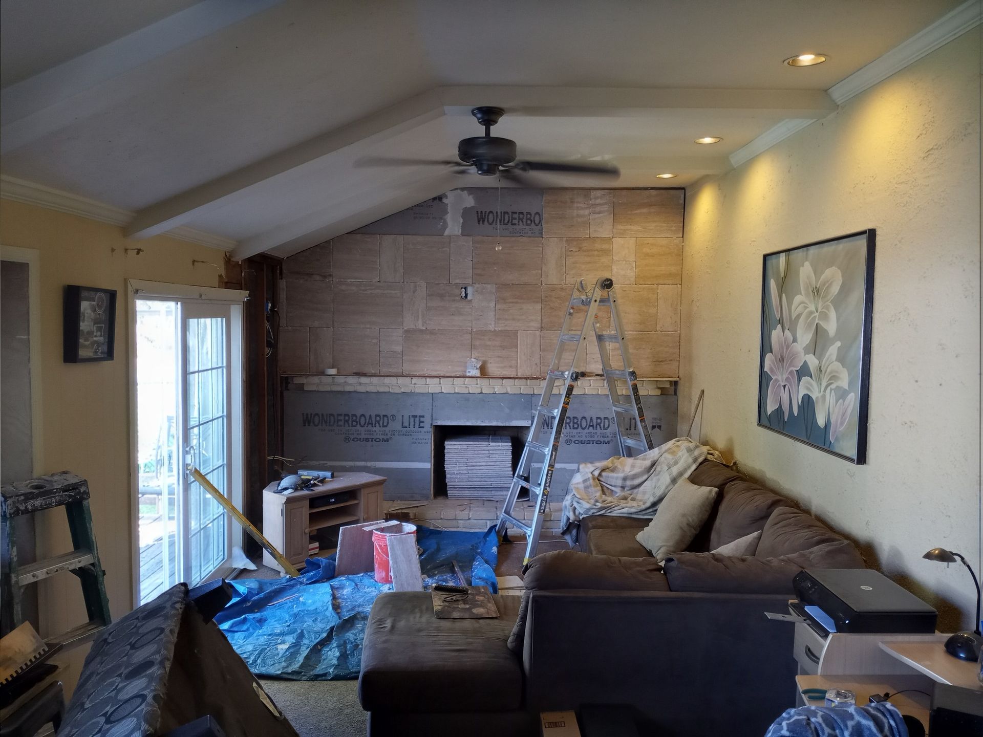 Living room under renovation with ladders, tools, and a brick fireplace wall