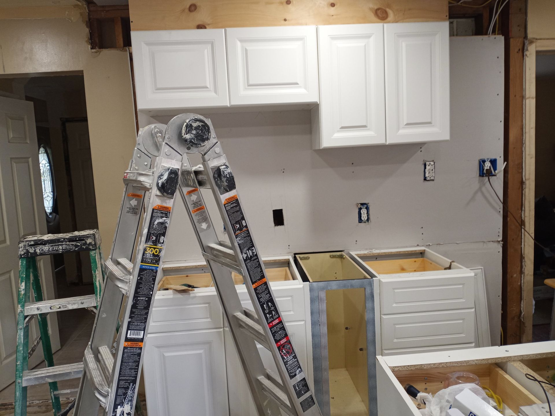 Kitchen renovation with cabinets removed, ladders, and exposed counters and wall outlets