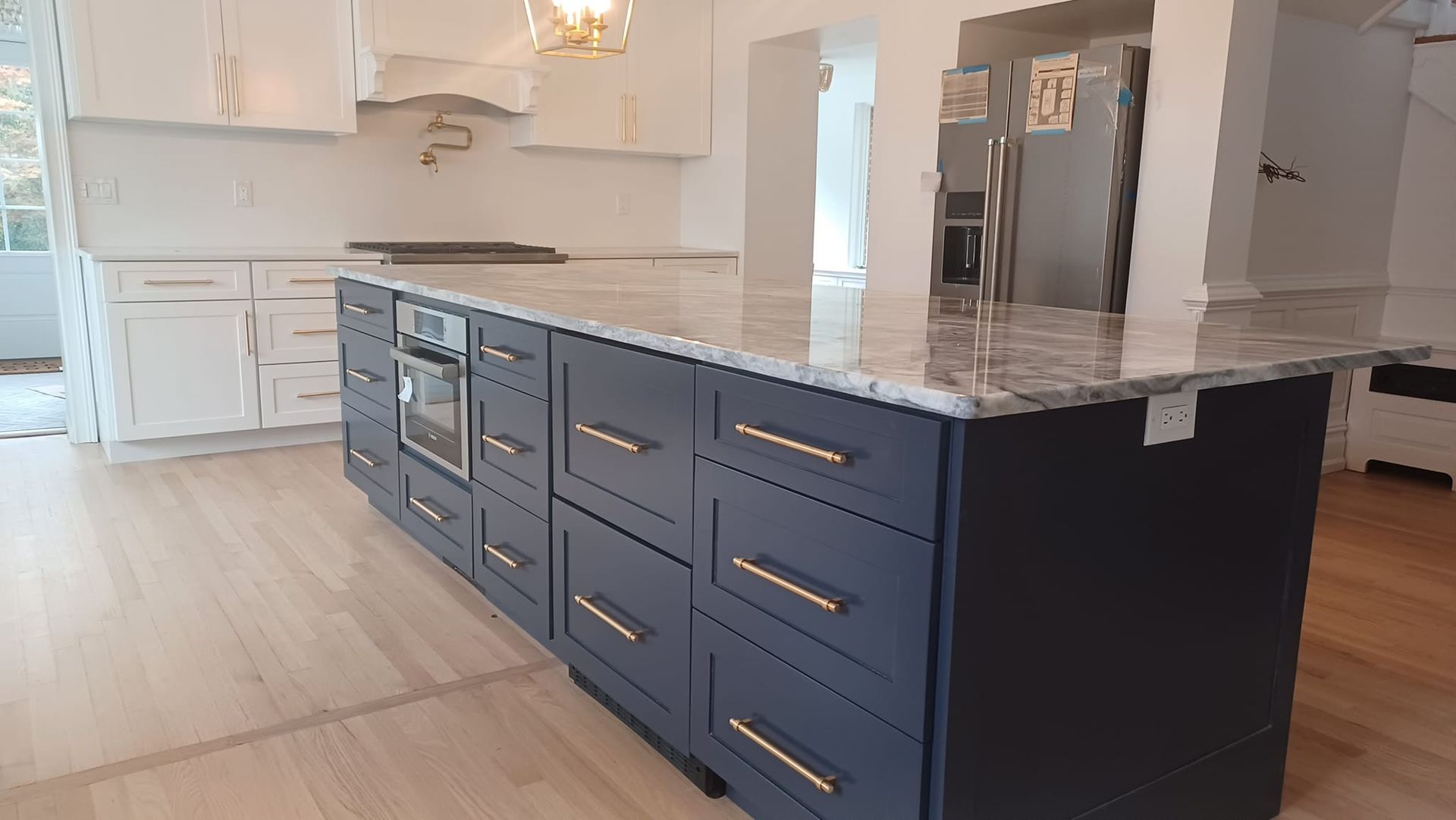 Modern kitchen with a navy island, white cabinets, marble countertops, and stainless steel appliances.
