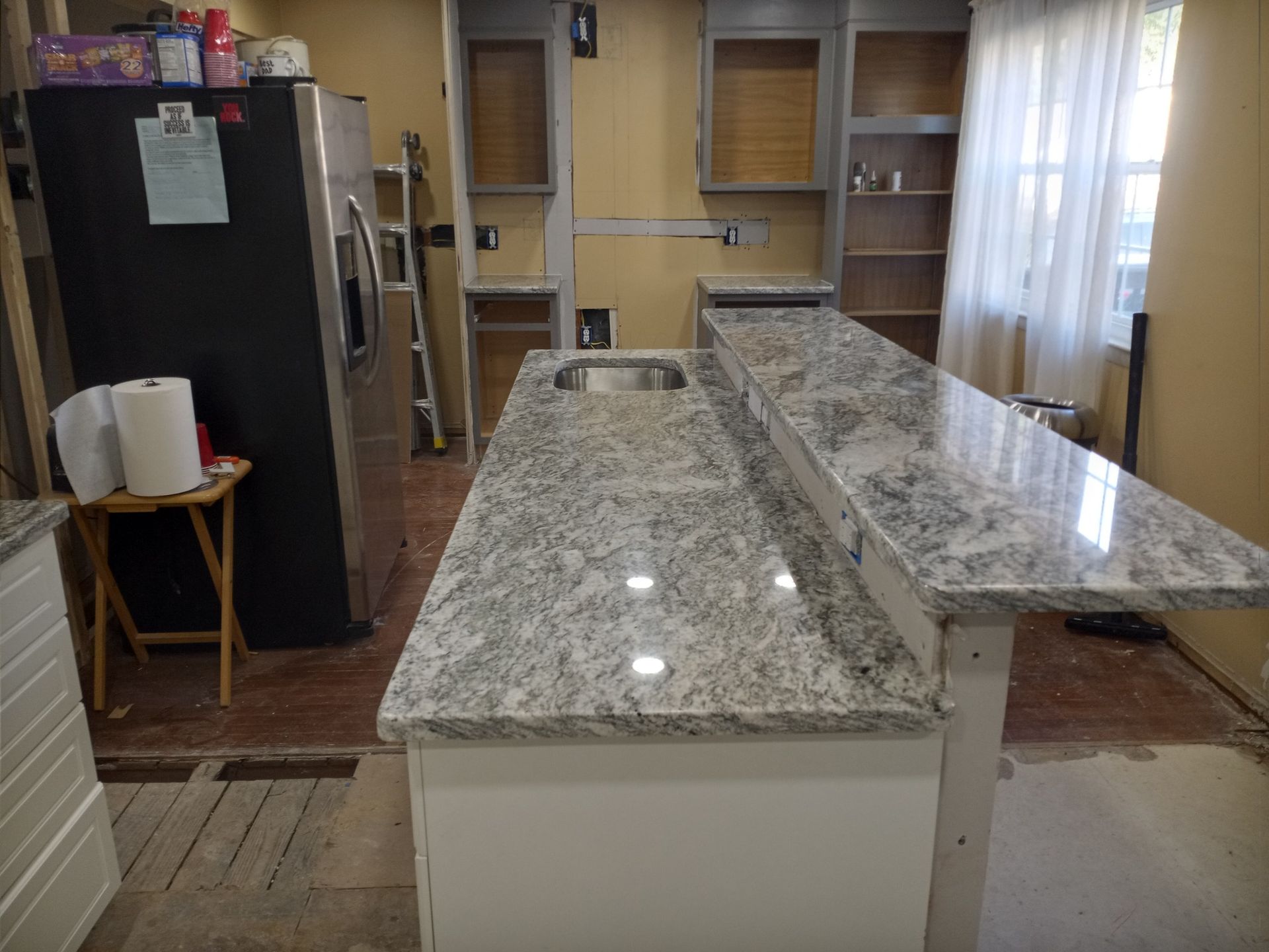 Modern kitchen with granite island, black refrigerator, and windowed dining area