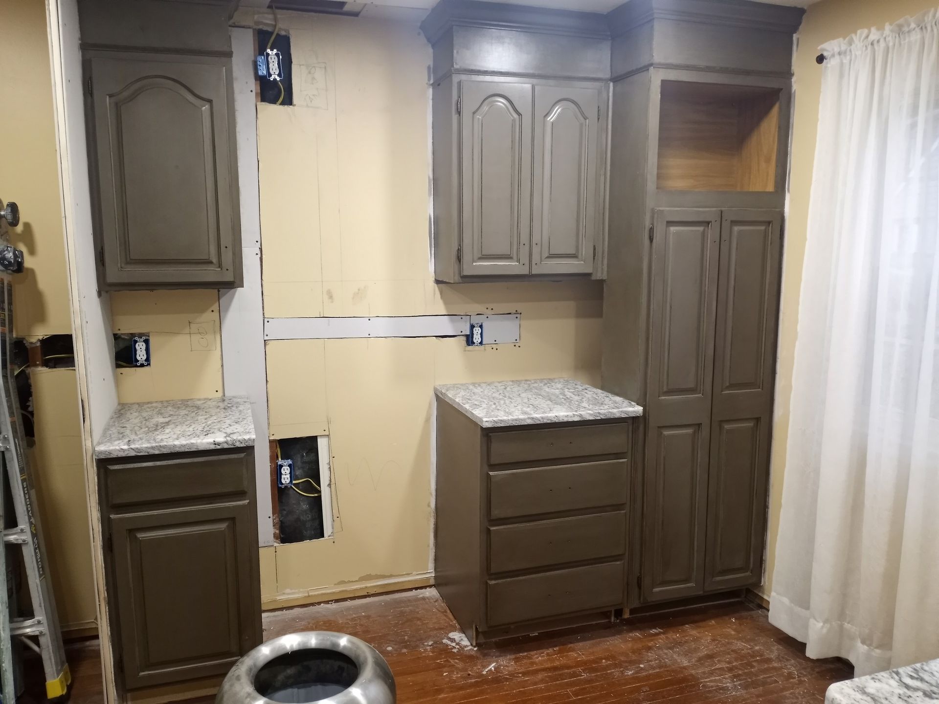 Kitchen with beige cabinets, granite countertop, and curtains, partially remodeled with exposed wall areas