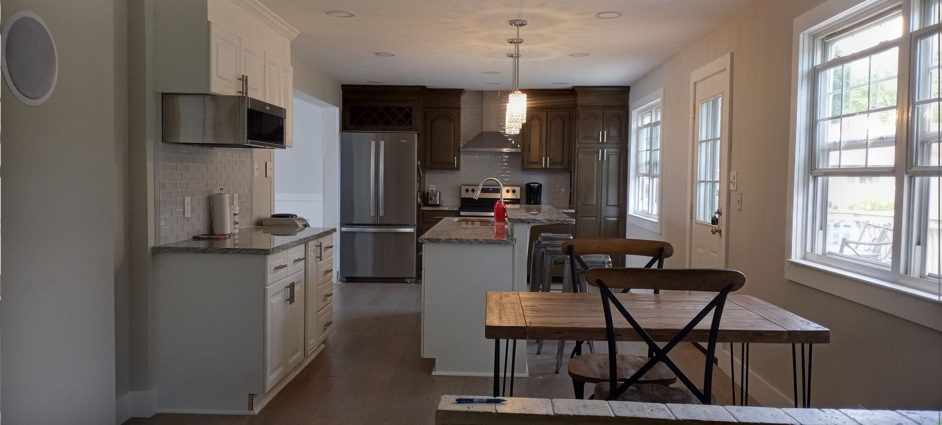 Bright kitchen-dining area with white cabinets, stainless fridge, wooden table, and large windows