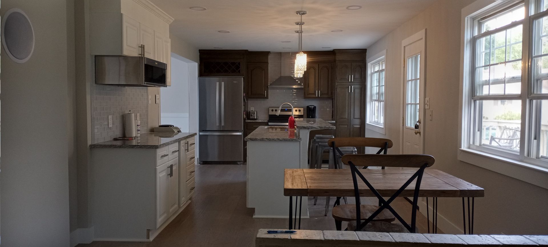 Bright kitchen and dining area with stainless fridge, dark cabinets, and large windows overlooking a table and chairs