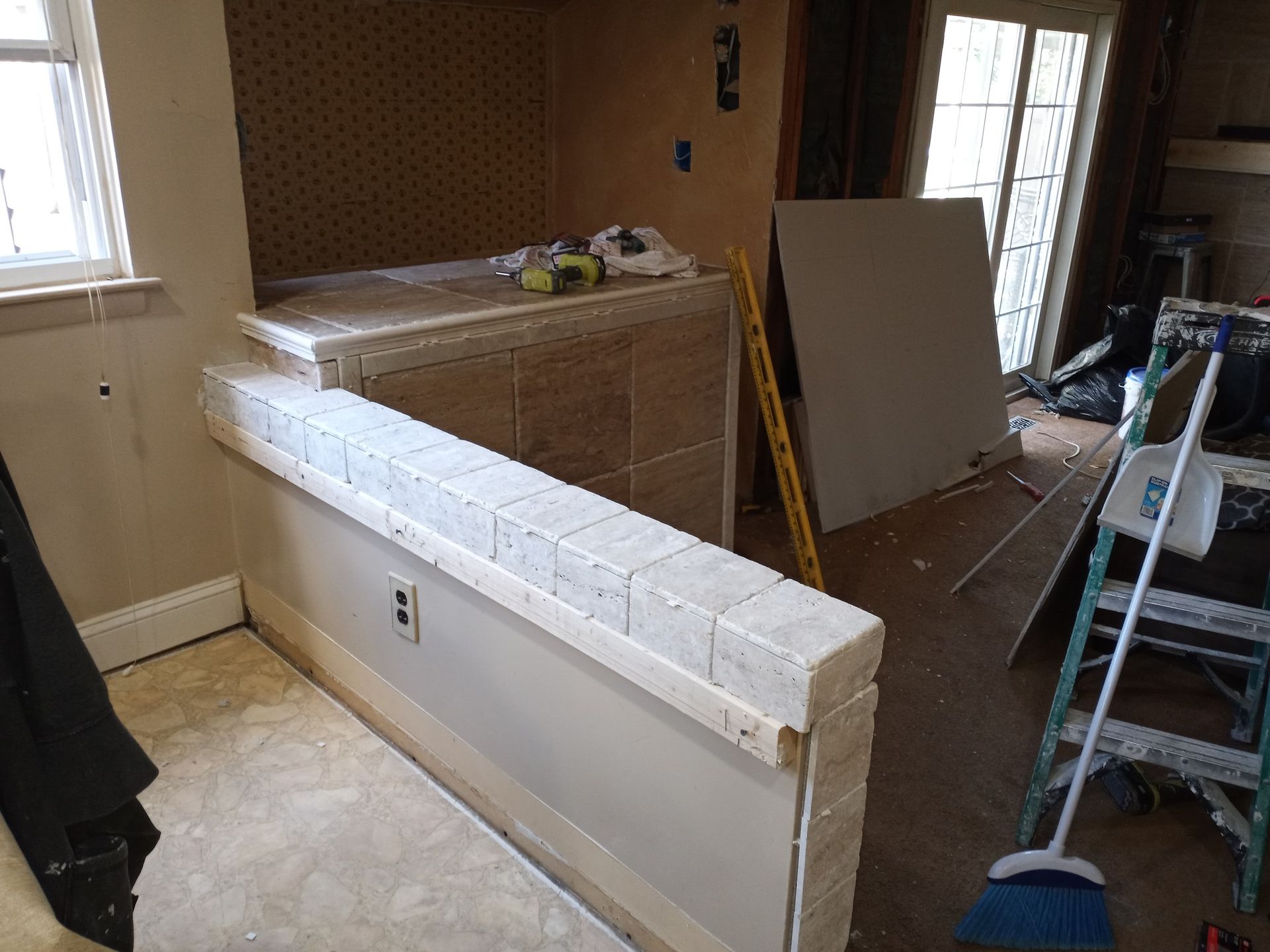 Living room under renovation with a half-built white half wall, ladder, and construction materials