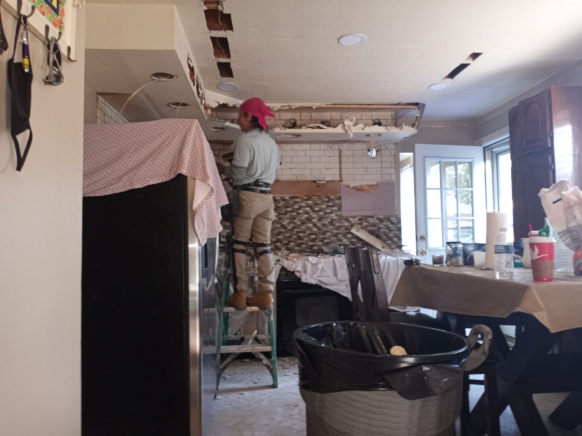 Person standing on a step ladder working on a partially demolished ceiling in a messy room