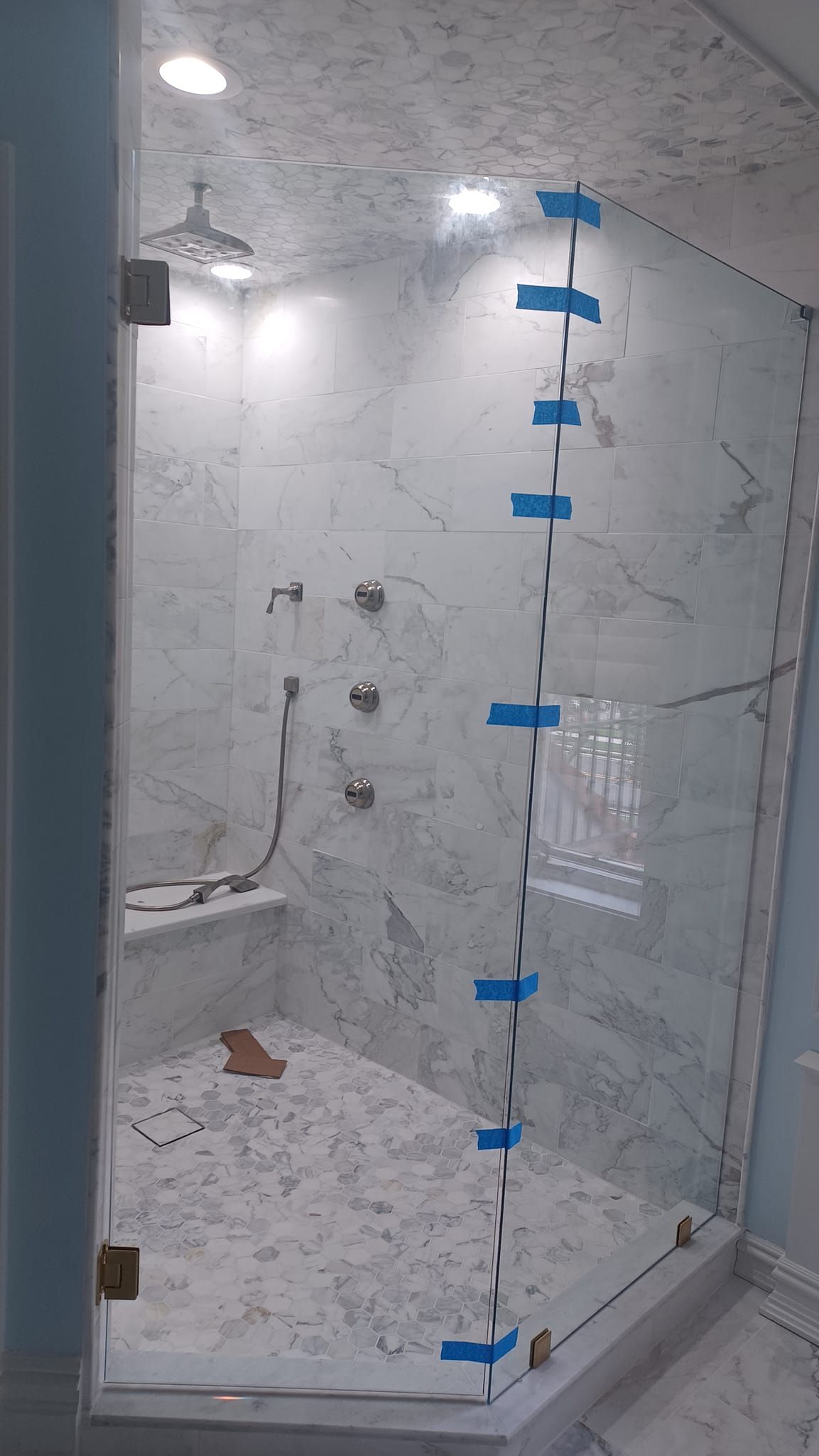 Bathroom shower under construction with tiled walls, glass partition, and blue painter’s tape markings