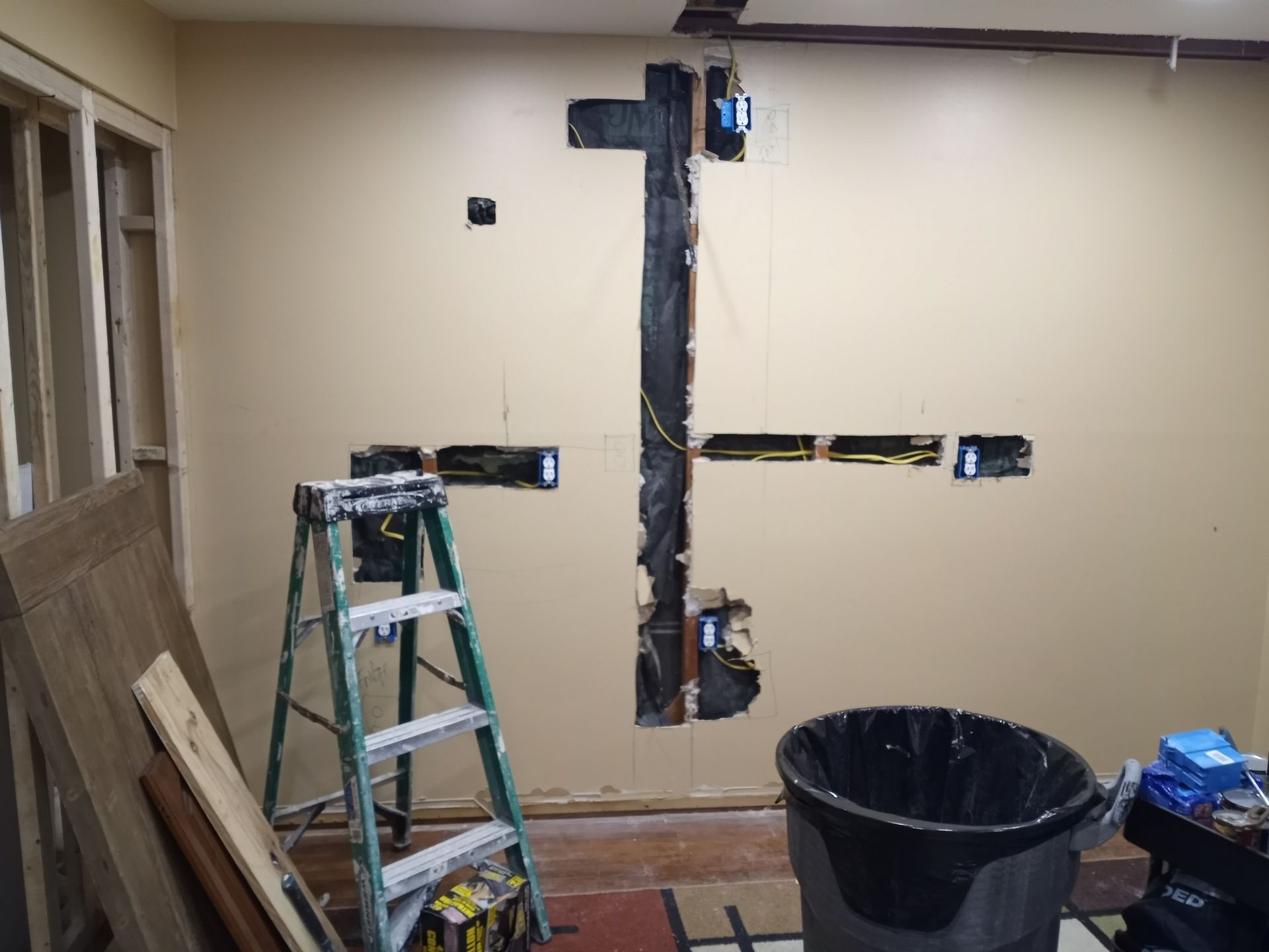 Partially renovated room with exposed wall wiring, ladder, and trash bin