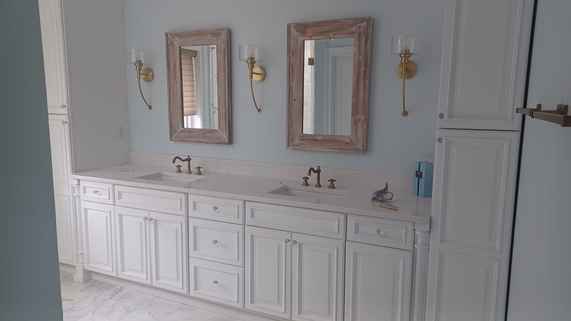 White bathroom vanity with double sinks, mirrors, sconces, and cabinet storage on a light blue wall