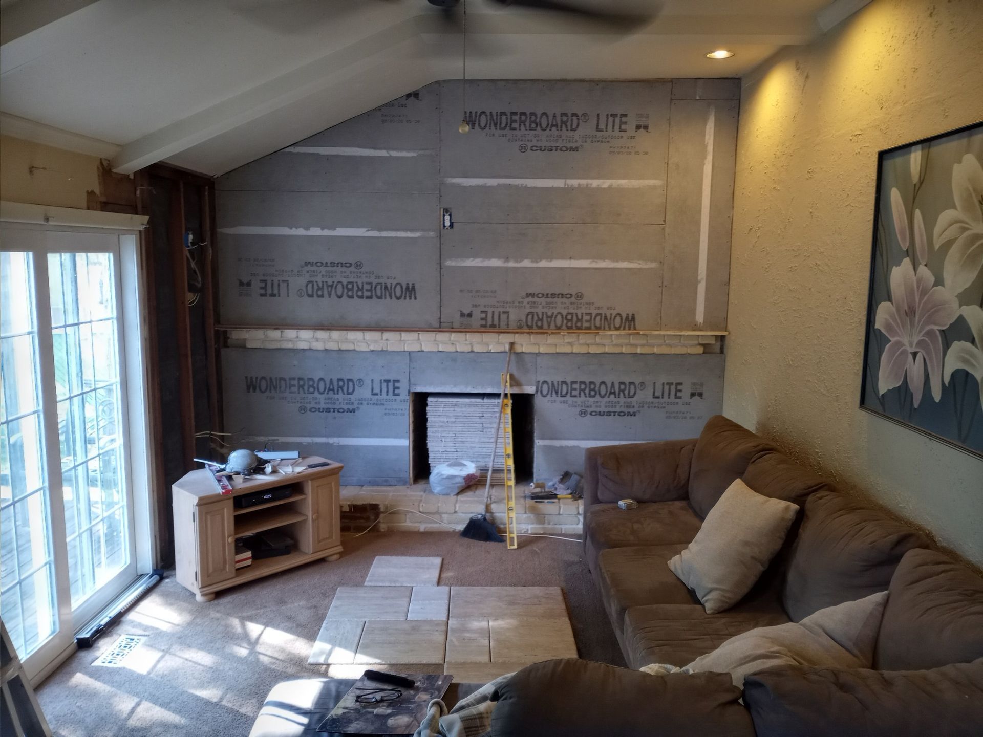 Living room under renovation with exposed wall insulation, sofa, TV stand, and sliding glass door