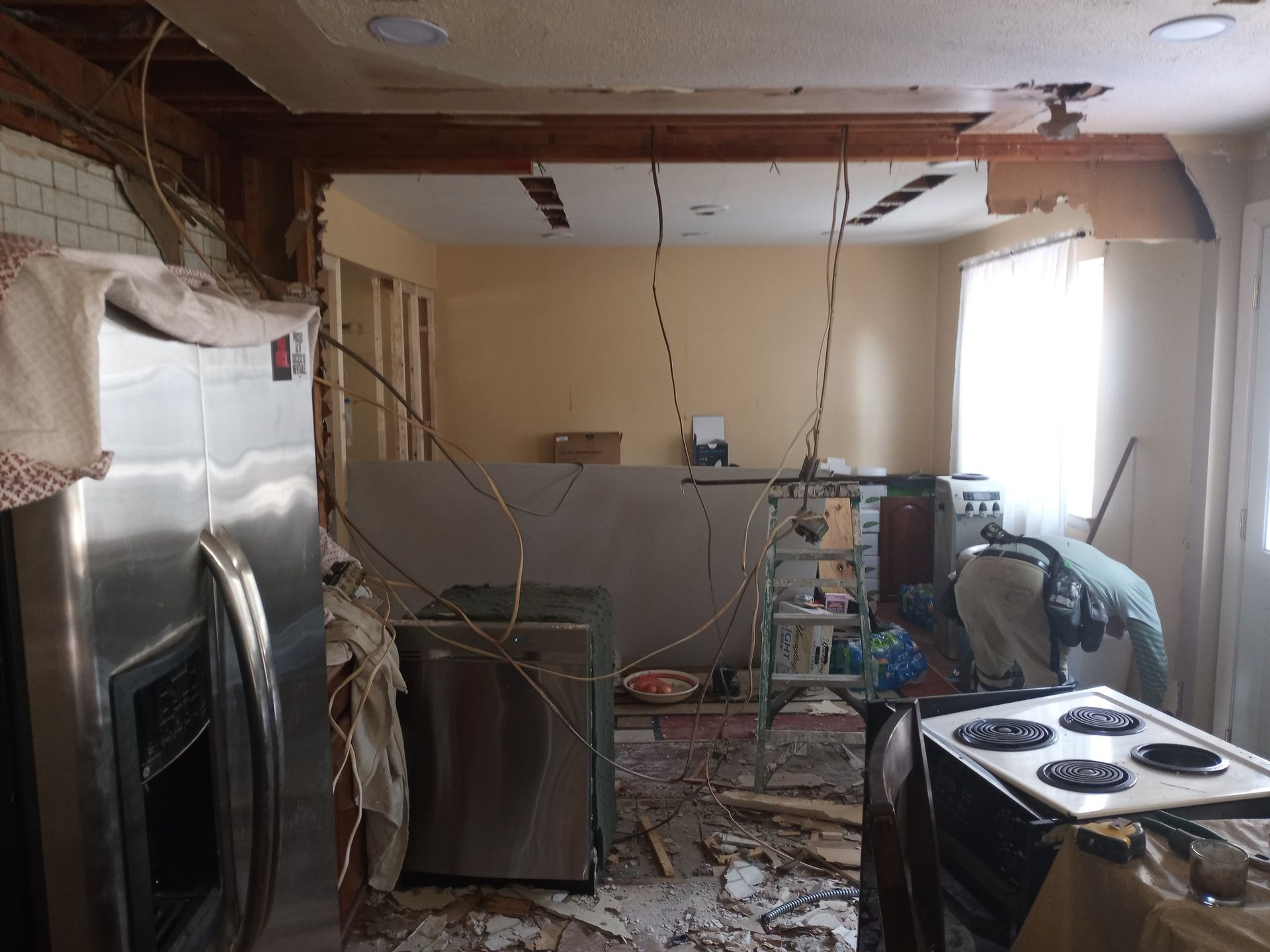 Damaged kitchen interior with debris, exposed ceiling, and broken appliances after demolition