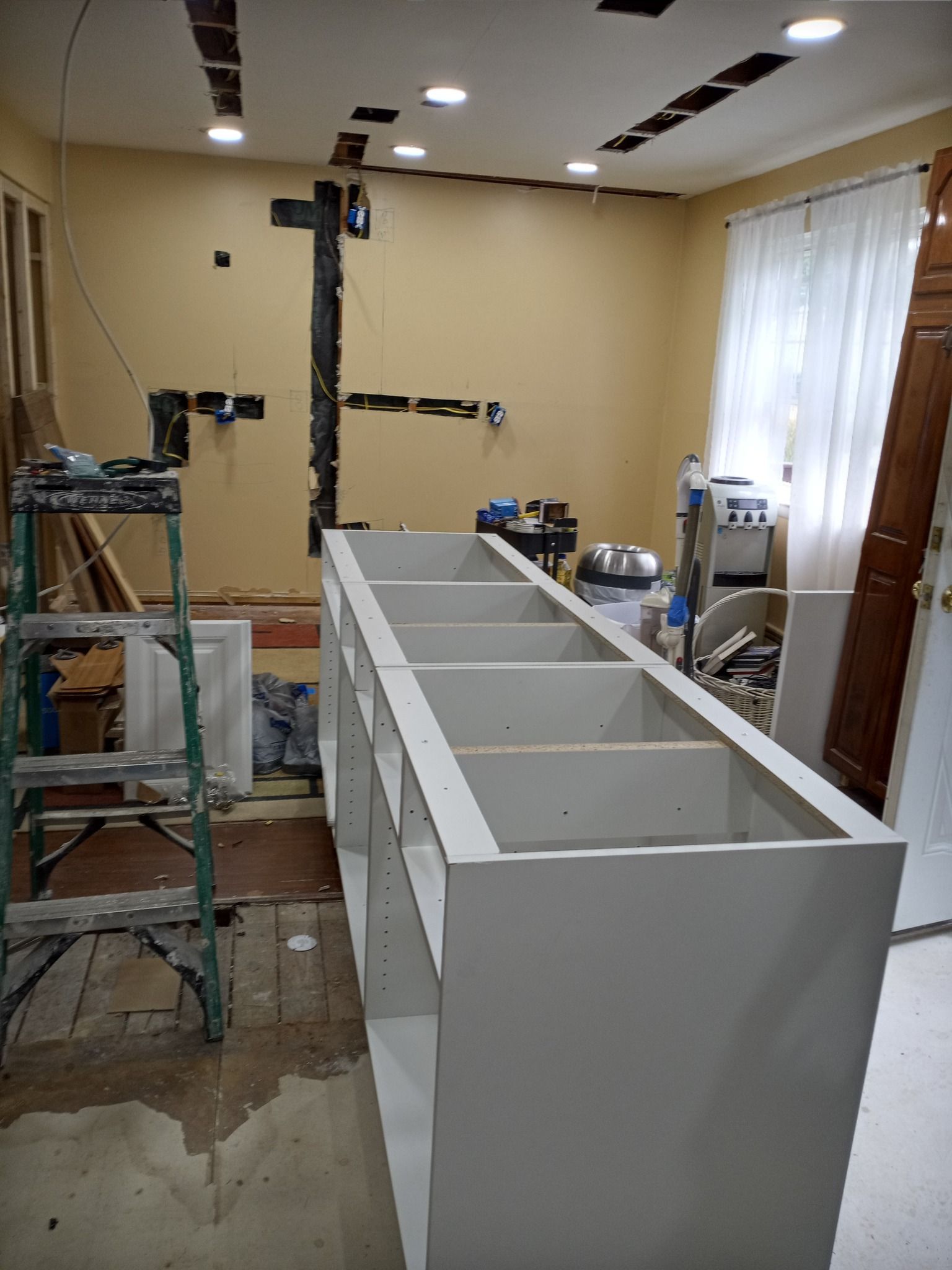 Unfinished white built-in cabinet in a room under renovation, with scaffolding and tools nearby.