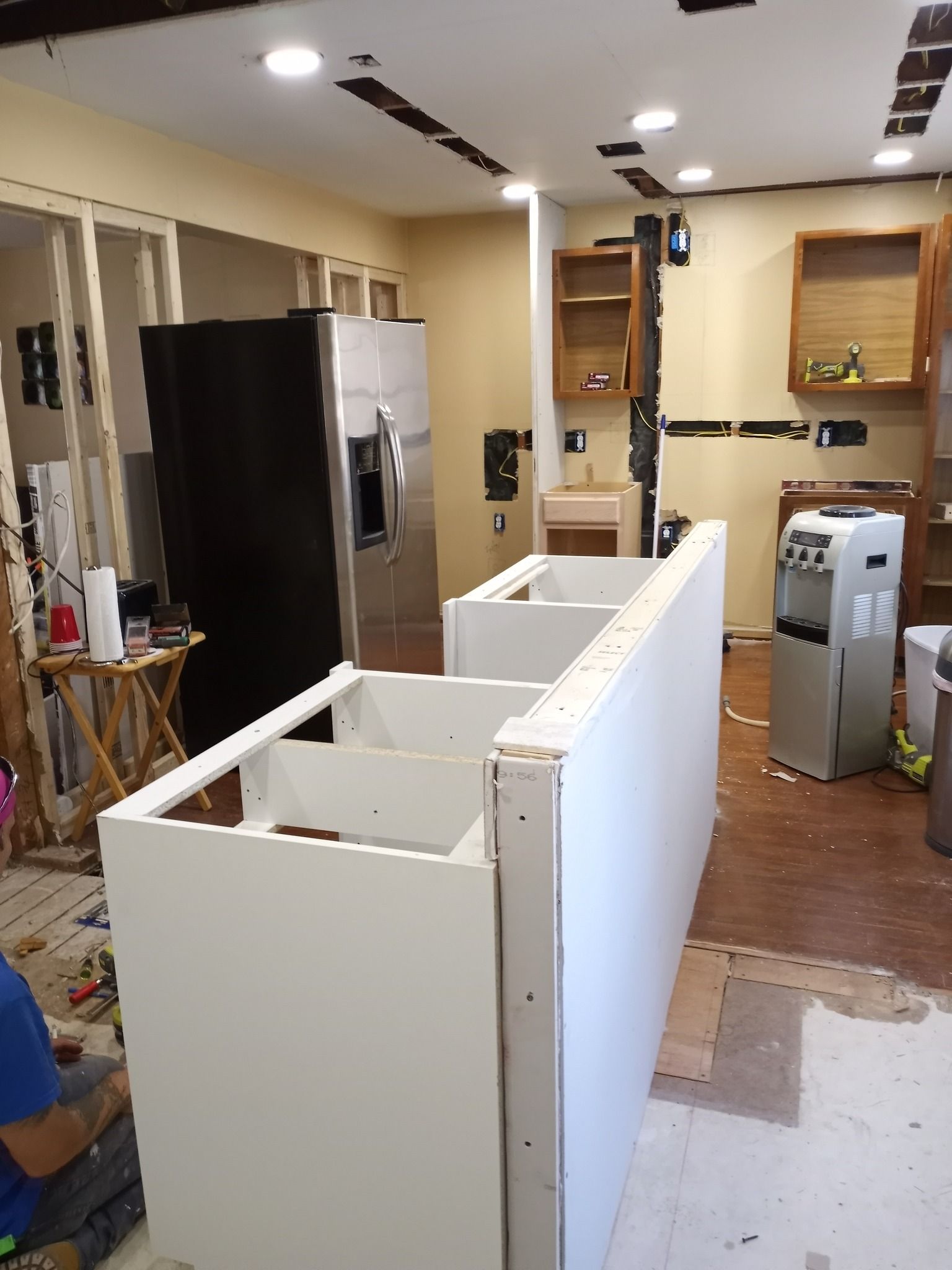 Kitchen under renovation with white cabinets, a black refrigerator, and exposed flooring