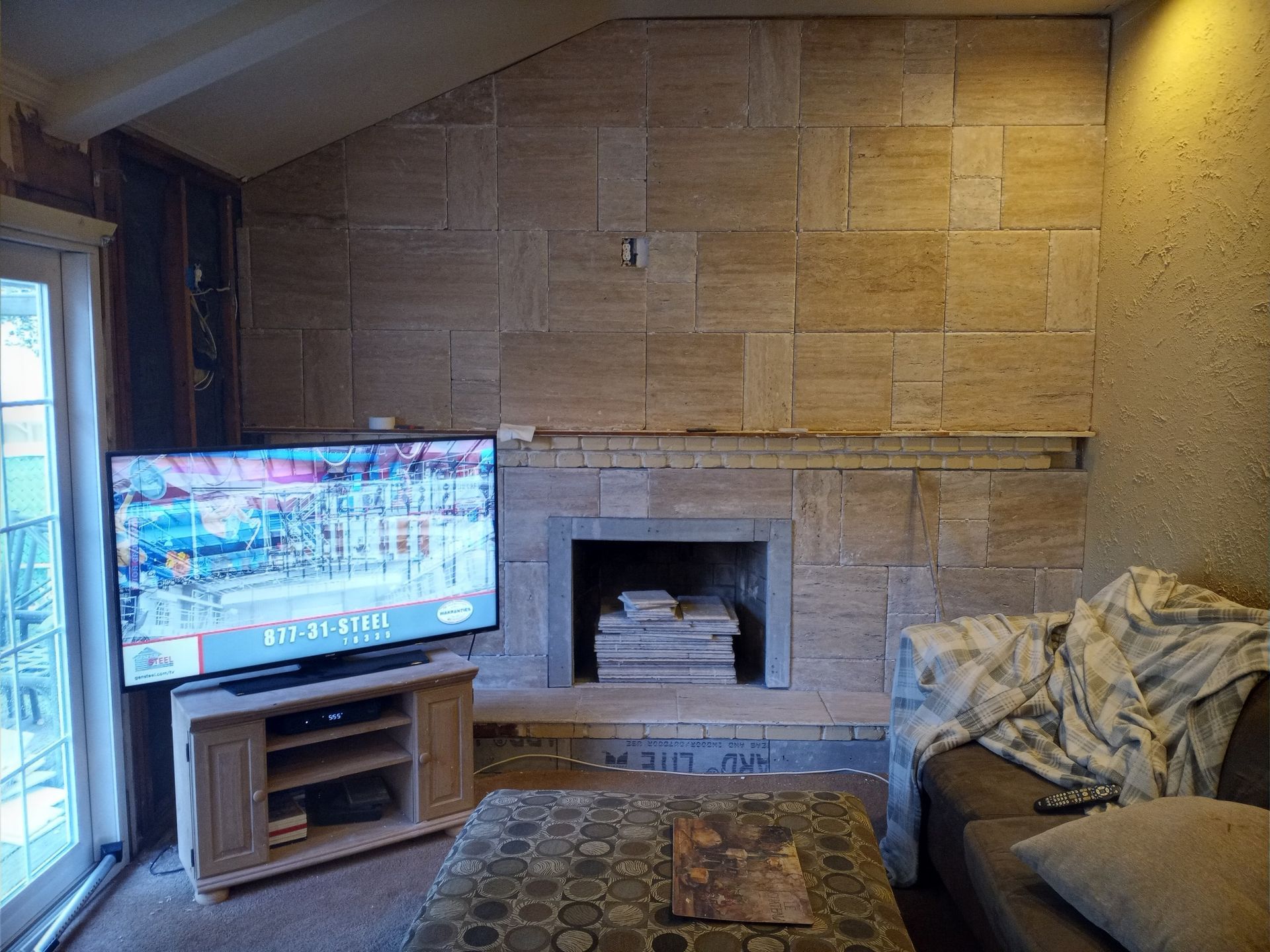 Living room with stone fireplace, TV, rug, and couch by a window