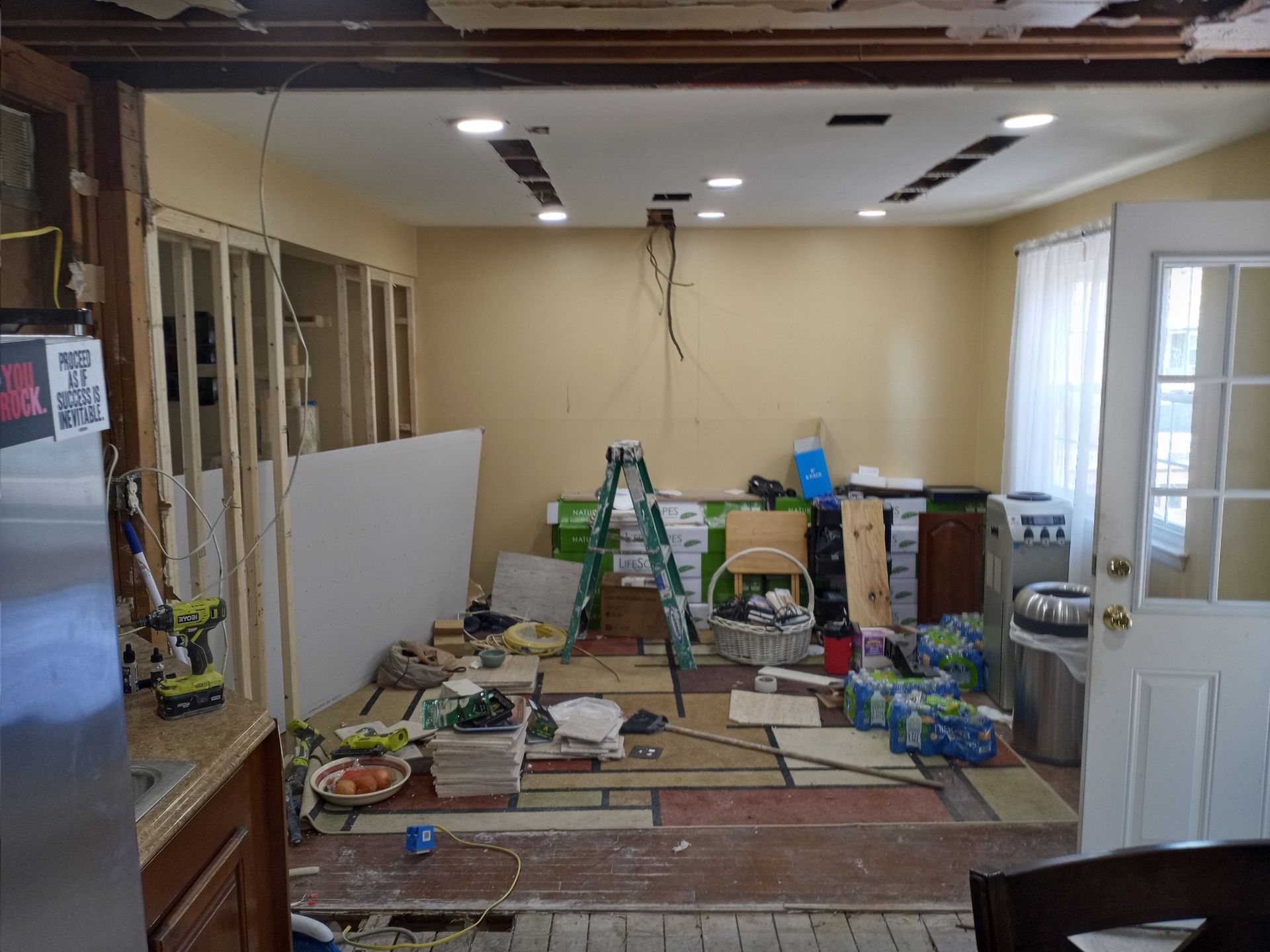 Partially renovated room with exposed wall studs, scattered tools, ladders, and construction materials