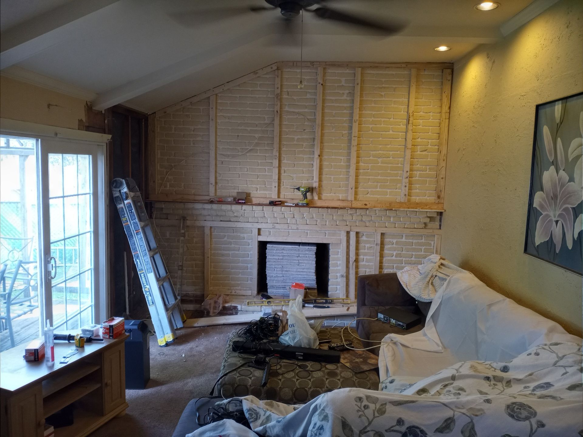 Living room under renovation with exposed wall framing, fireplace, ladder, and covered furniture