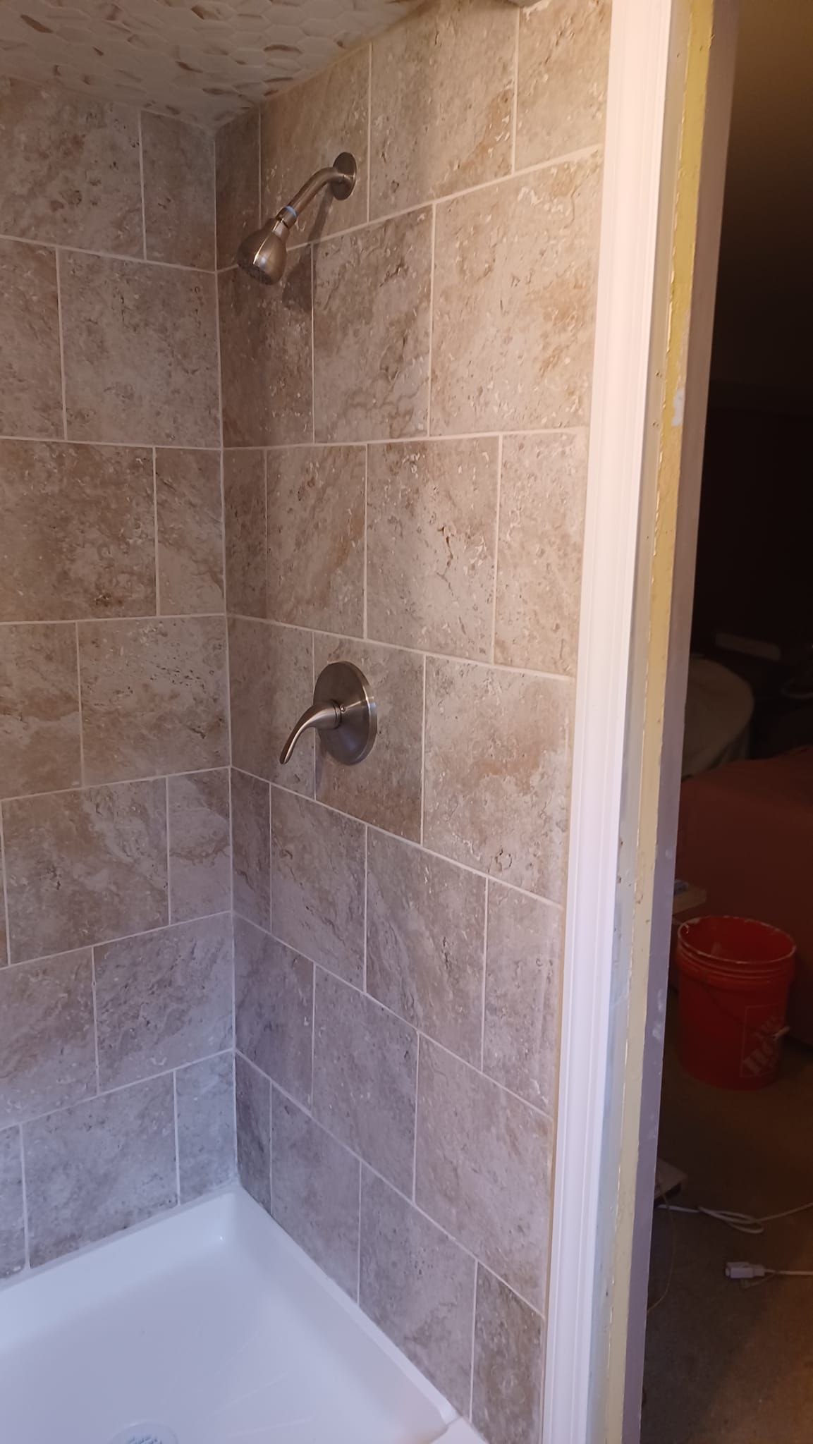 Tile shower corner with two wall-mounted showerheads and a white bathtub below, next to an open doorway