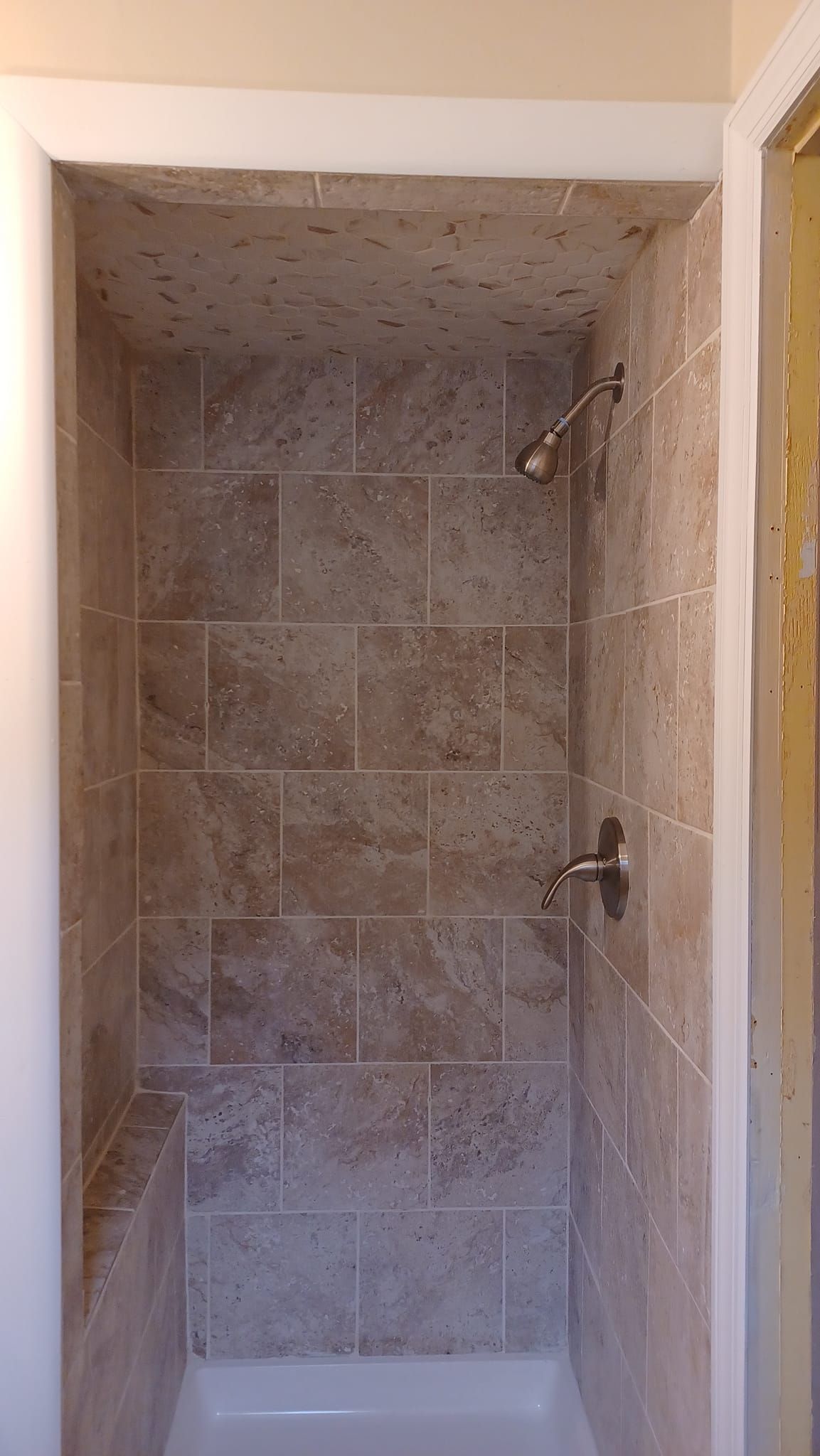 Narrow tiled shower stall with beige walls, chrome shower fixtures, and a white tub floor.