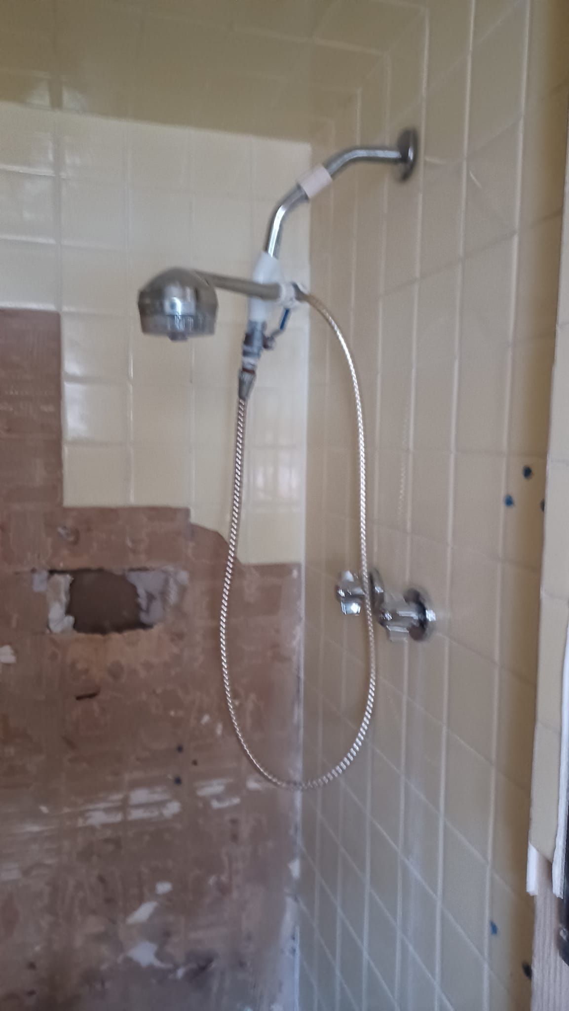 Tiled bathroom shower with handheld showerhead and exposed wall repair area