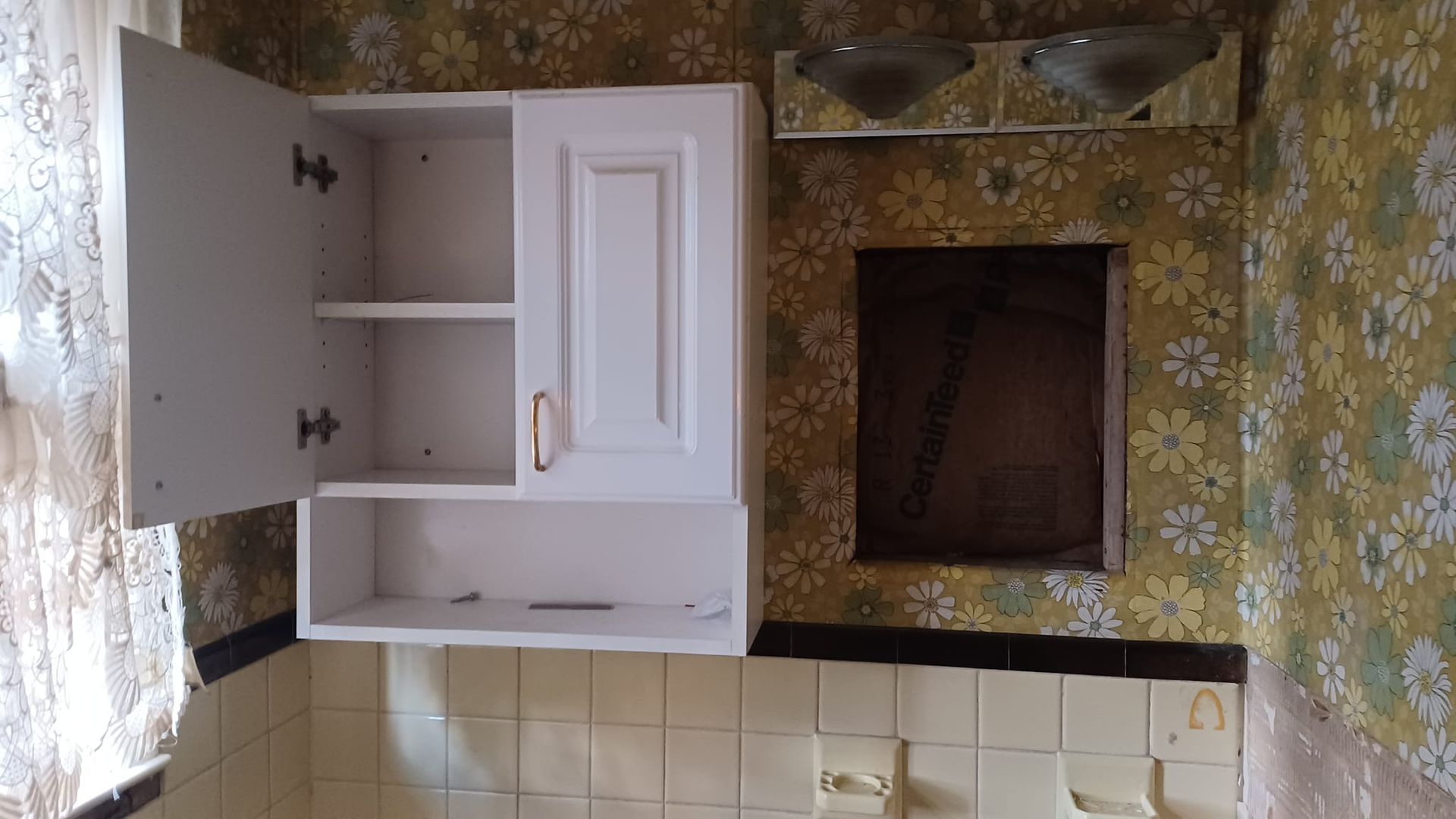 Open bathroom vanity cabinet with white doors and shelves, beside a tiled sink and mirror area.