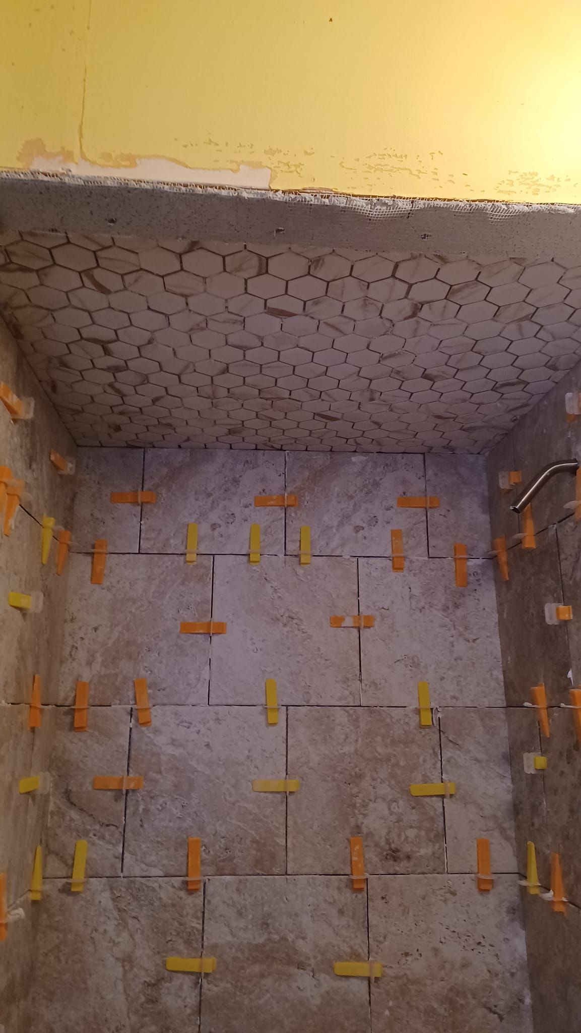 Small tiled room with gray walls, patterned ceiling, and yellow clips or spacers along the edges