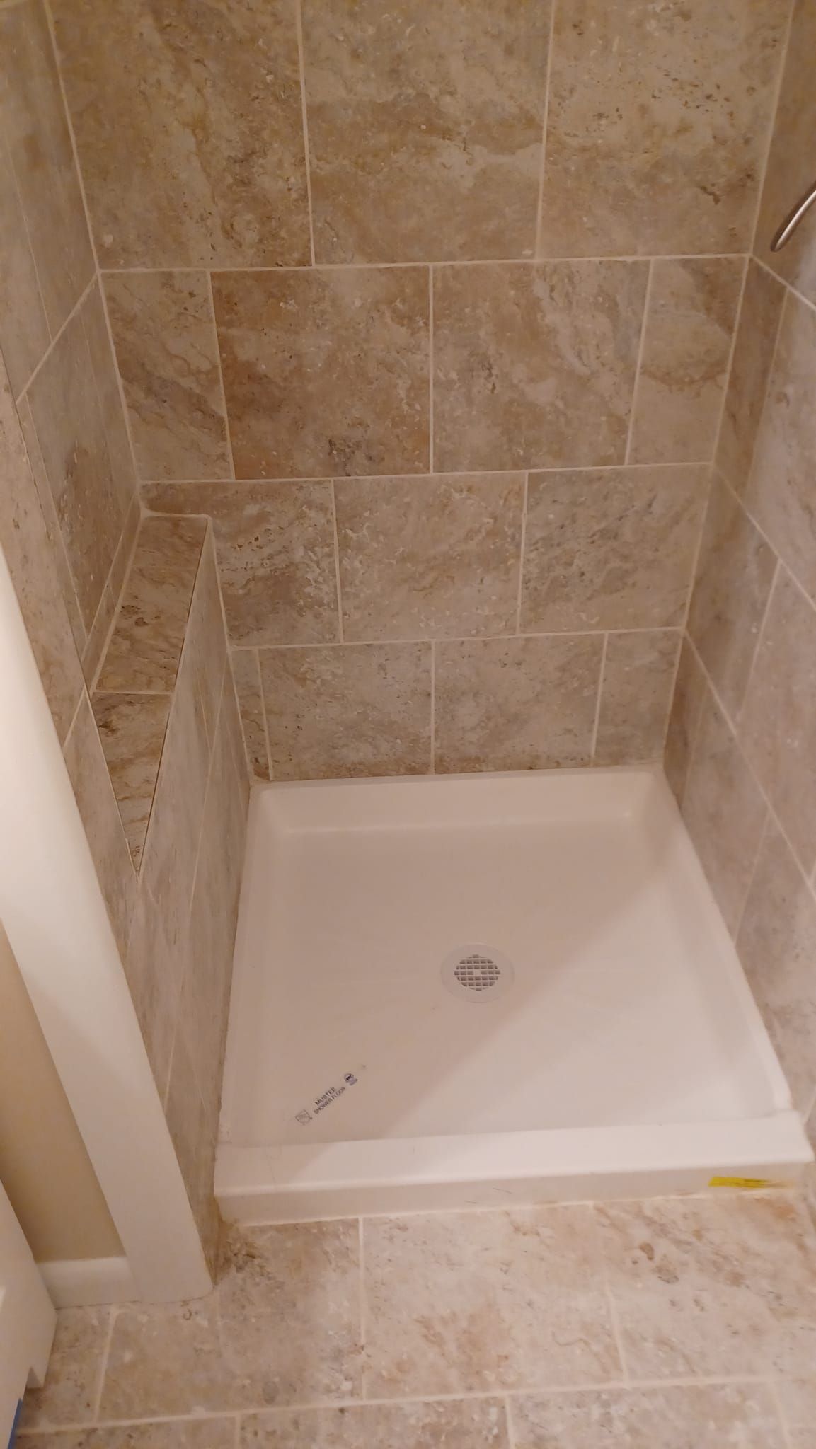 Small beige-tiled shower stall with a white shower pan and drain.