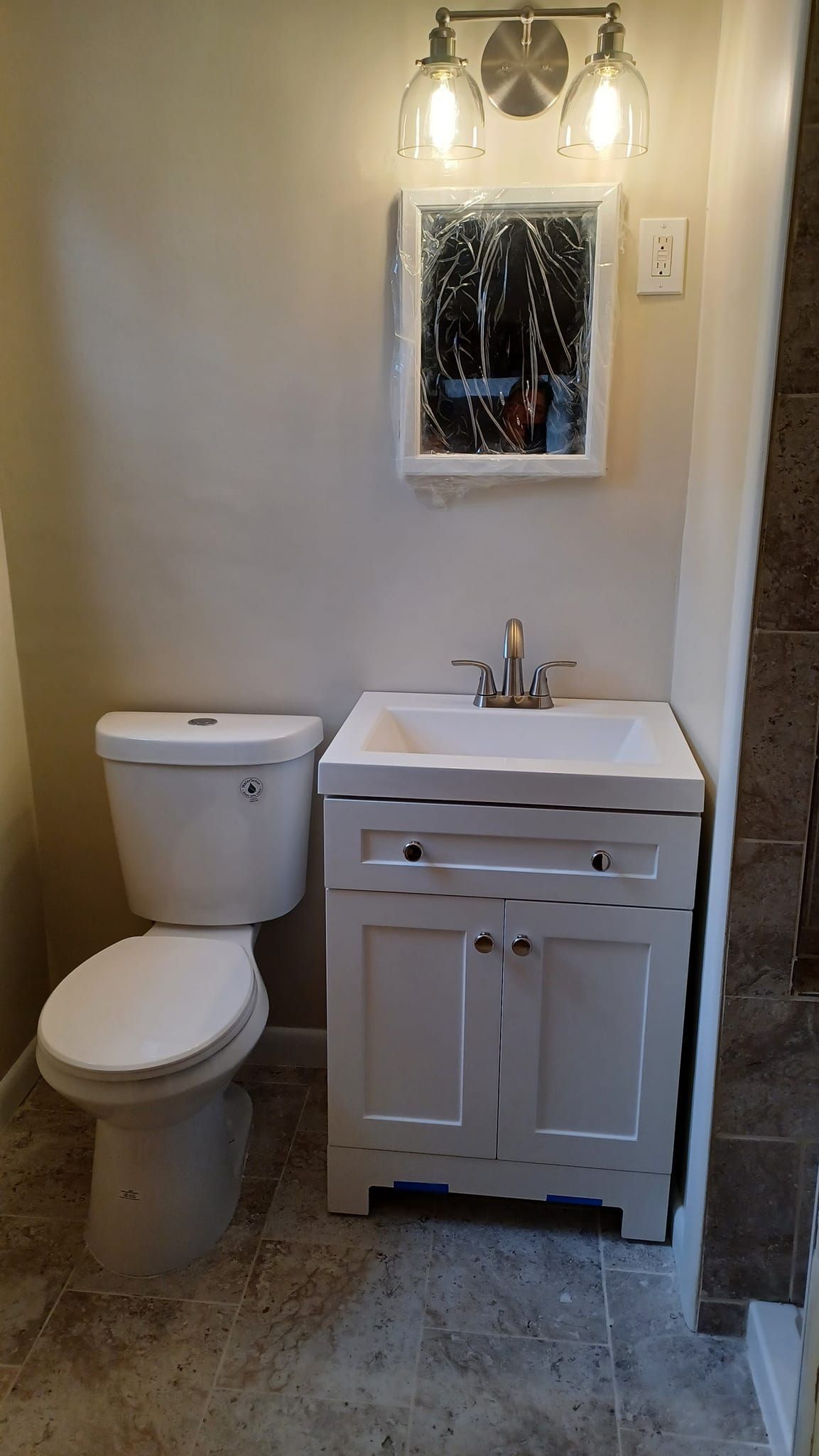 Small bathroom with toilet, white vanity sink, mirror, and light fixture.