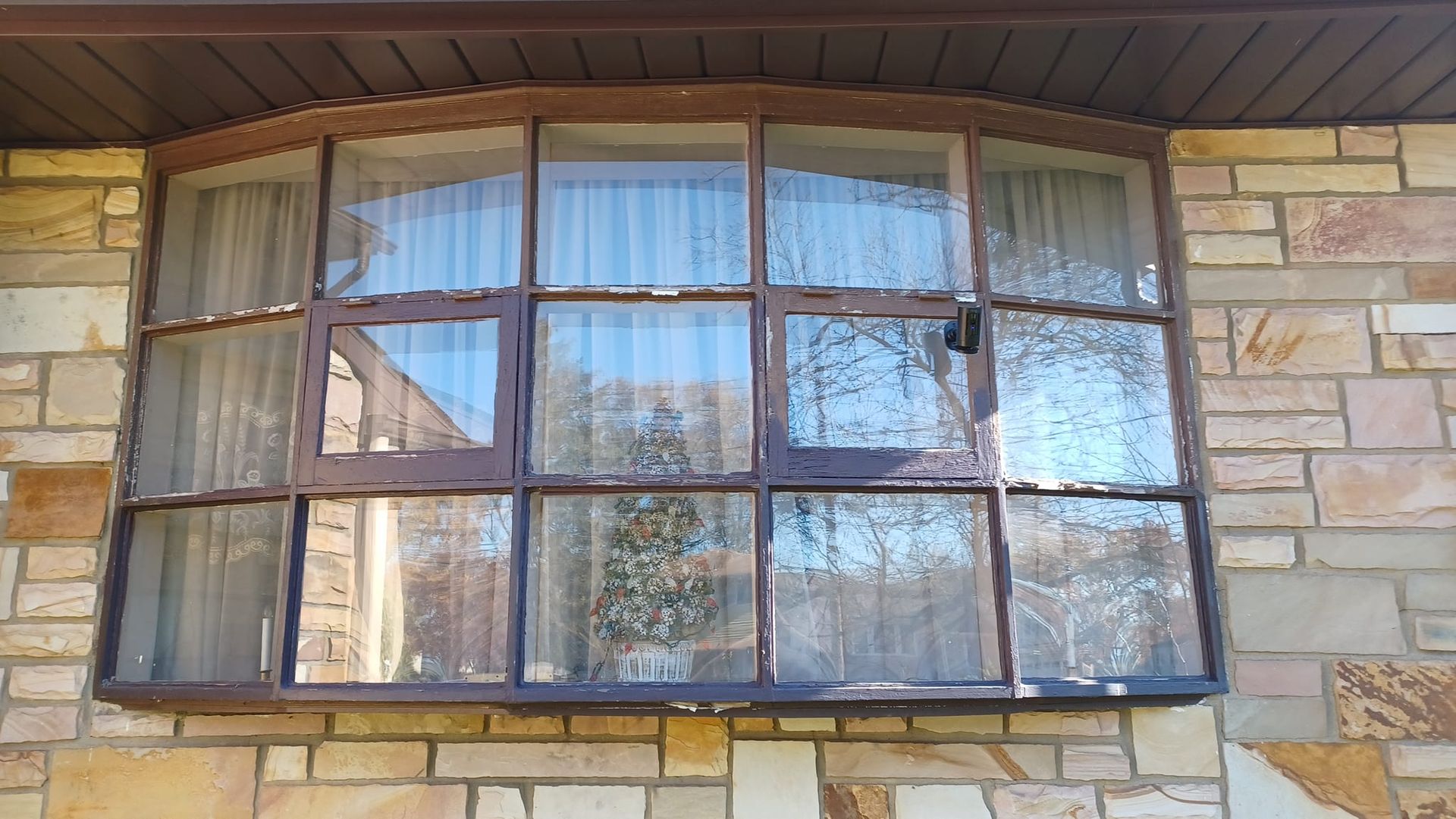 Curved bay window with reflective panes set in a stone exterior wall under a roof overhang