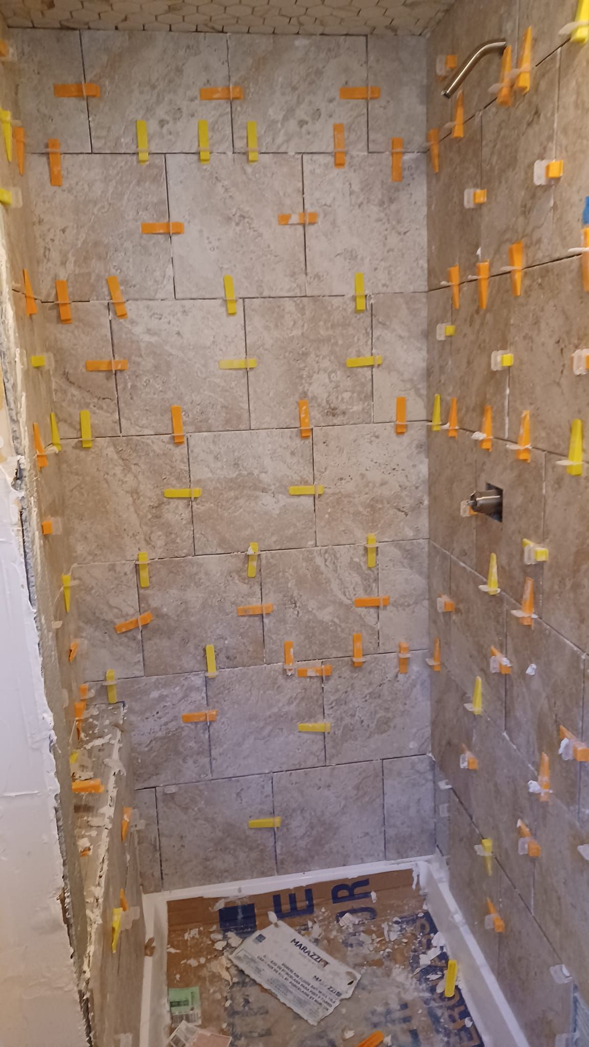 Narrow unfinished stairwell with gray concrete walls and orange tile spacers, viewed from above.