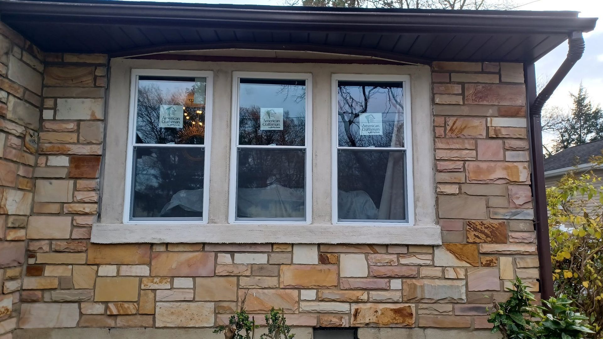 Stone house exterior with a white-framed three-pane window beneath a roof overhang