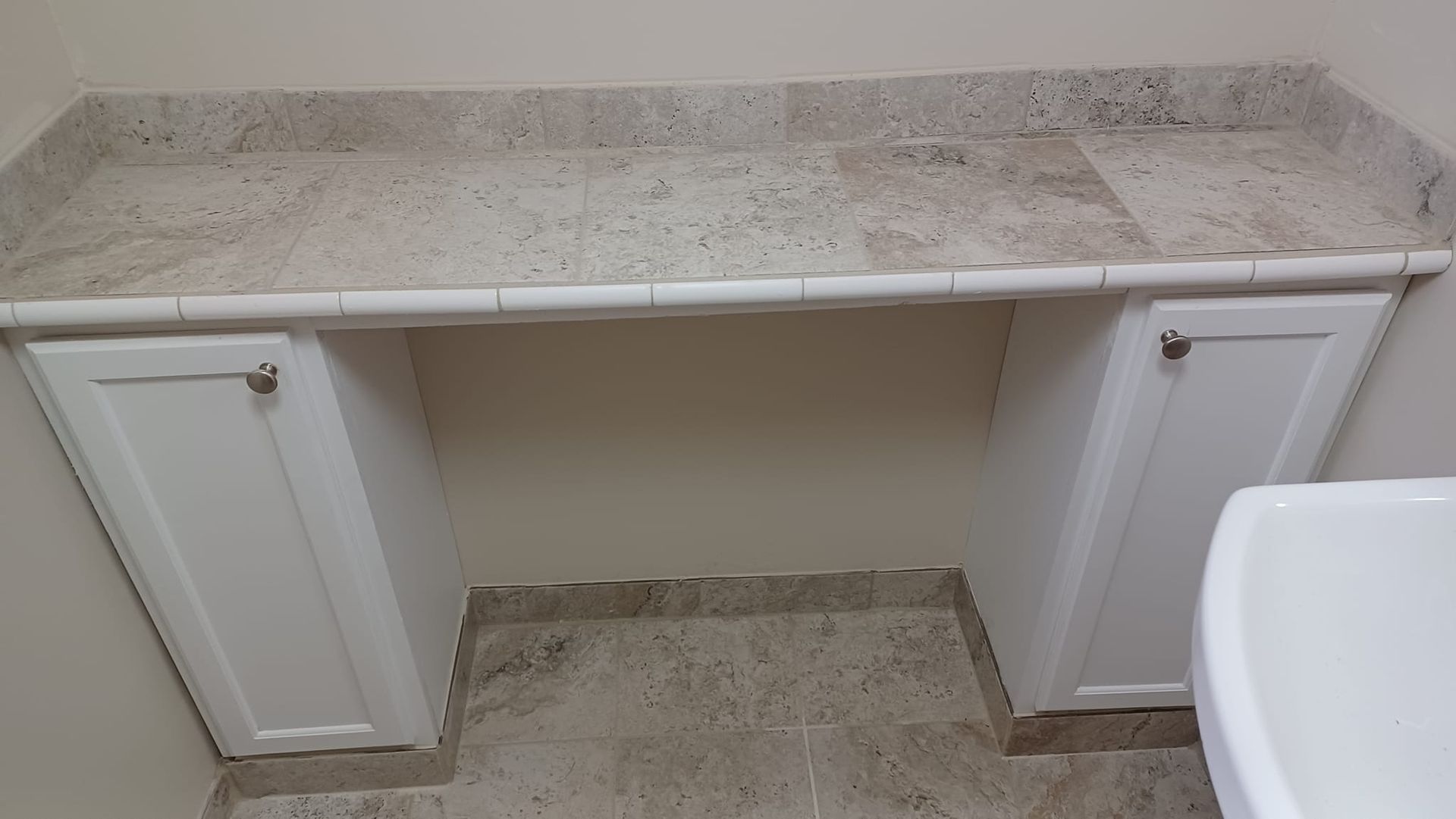 Bathroom vanity with a beige stone countertop and white cabinets under a mirror