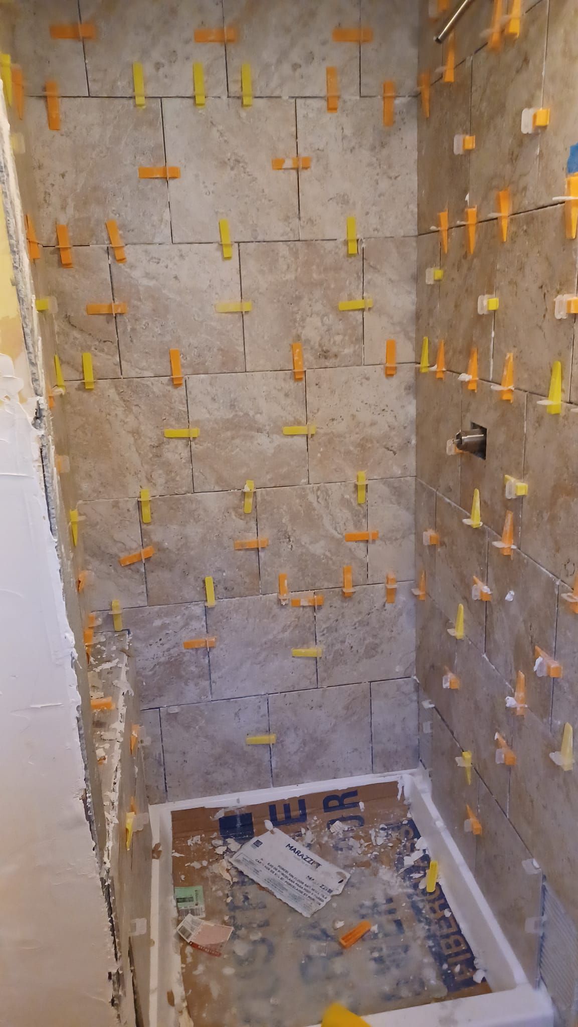 Tiled shower stall under construction with unfinished concrete walls and yellow spacers.