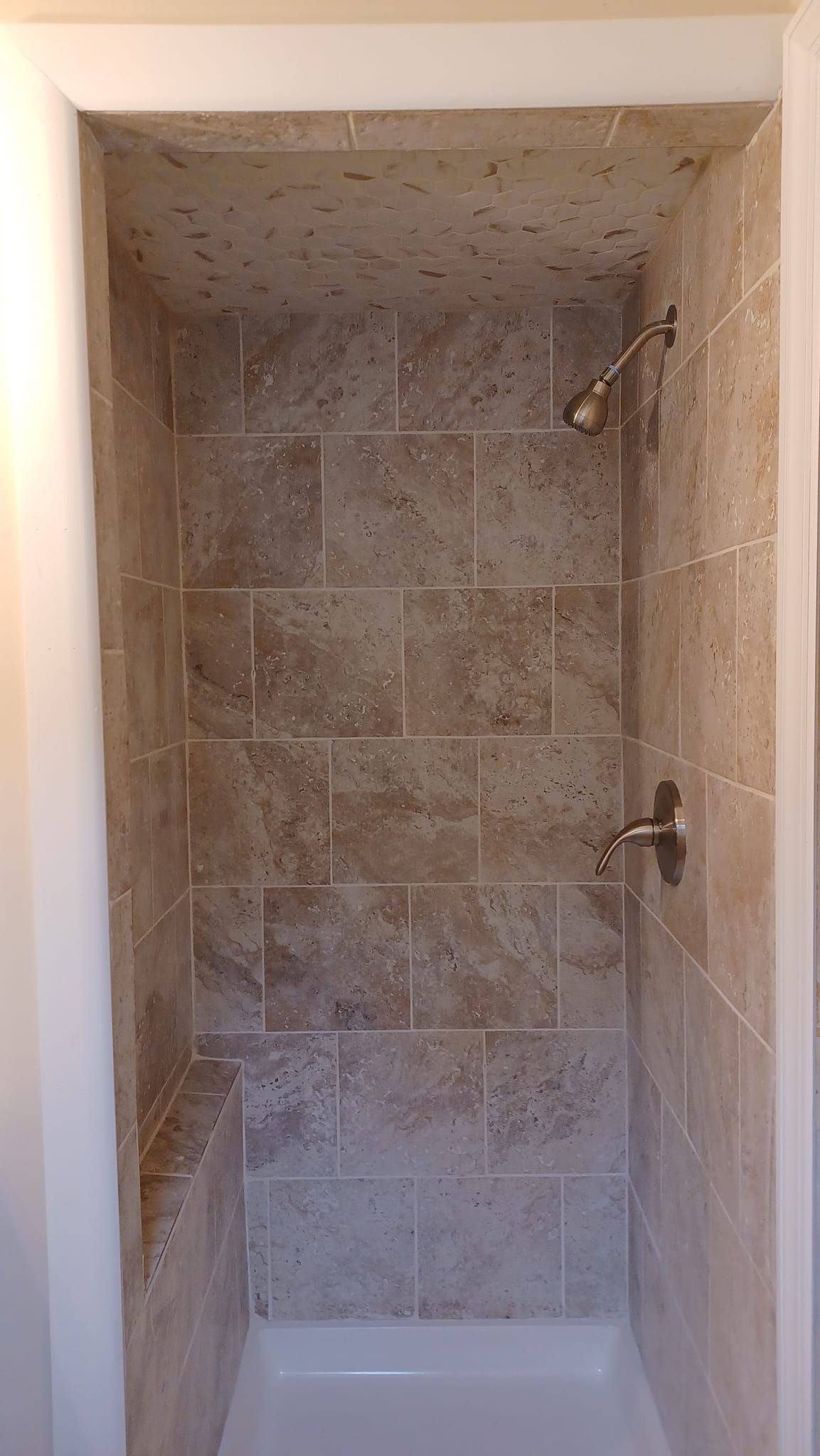 Small tiled shower stall with two wall-mounted fixtures and a white tub base