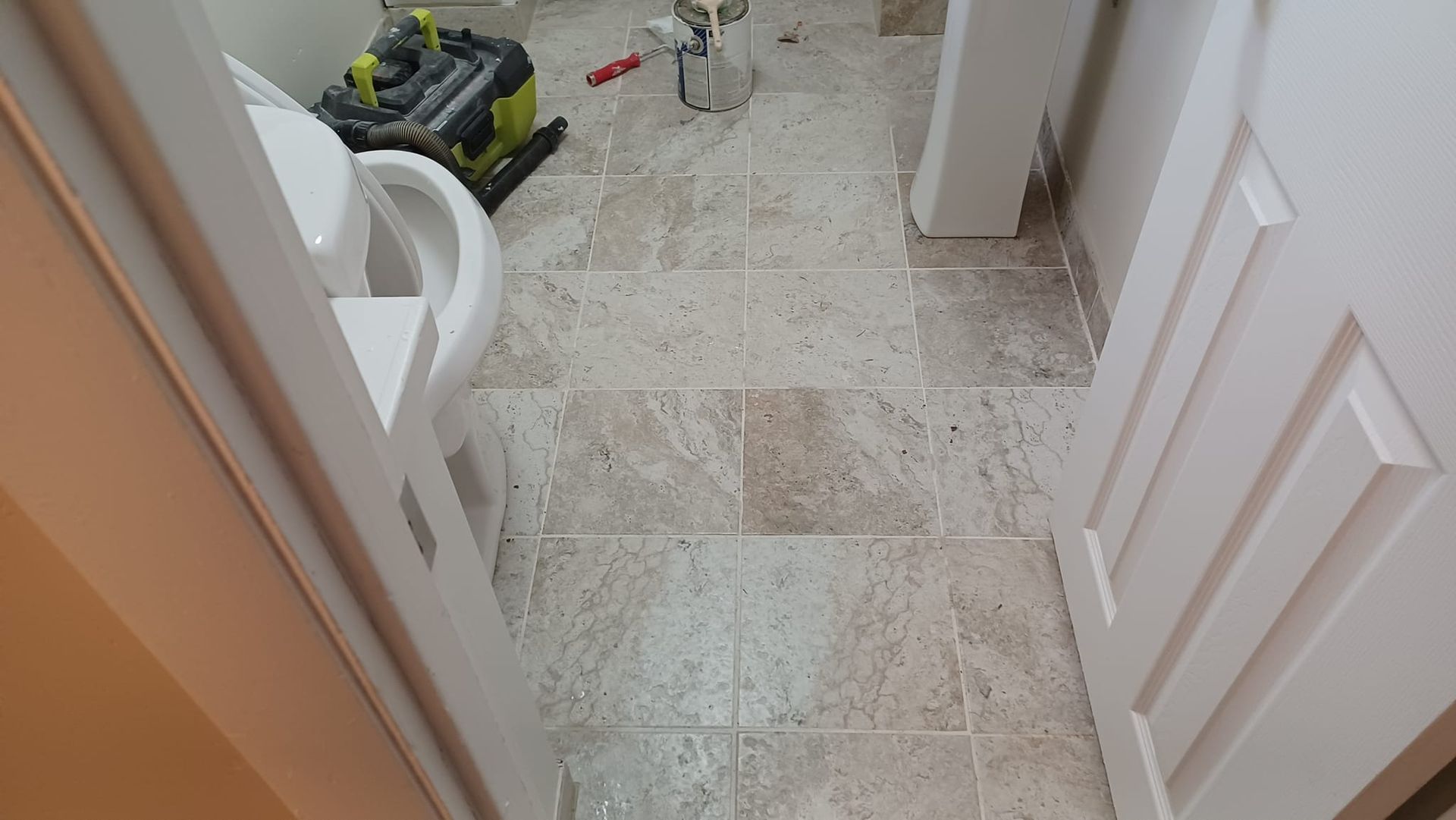 Bathroom floor with tile and a robotic vacuum near the toilet and open door.