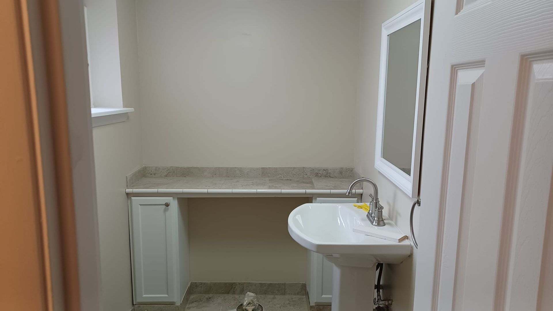 Small unfinished bathroom with white sink, vanity, and countertop beside a doorway.