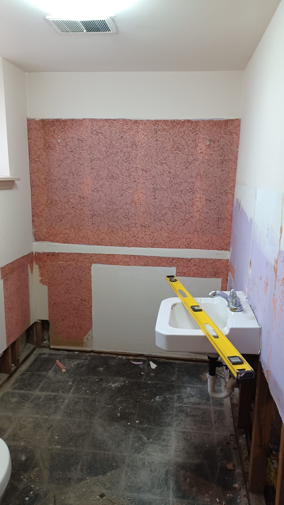 Small room under renovation with exposed walls, dark floor, and a sink with yellow support braces.