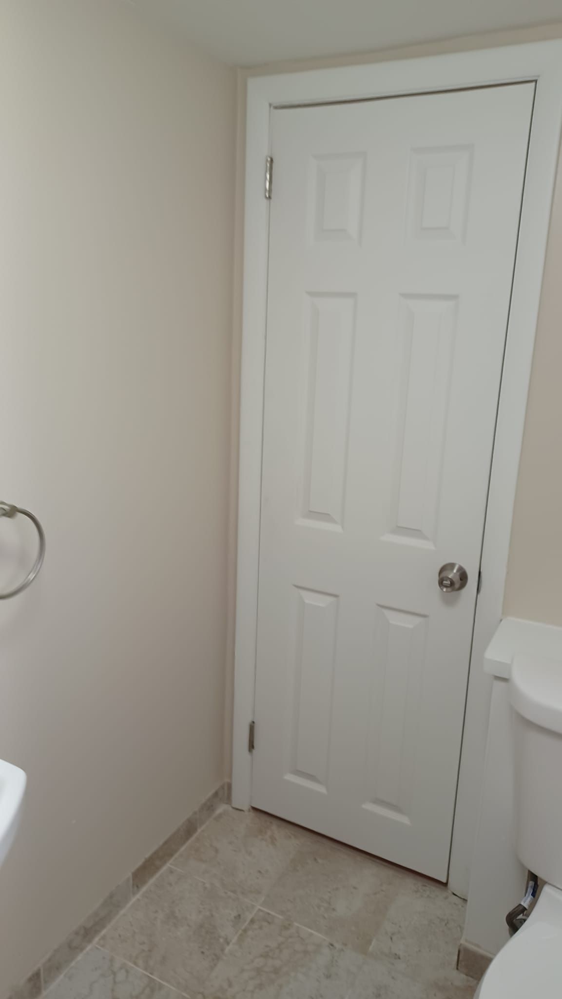 Small beige bathroom with a white paneled door and light tile floor.